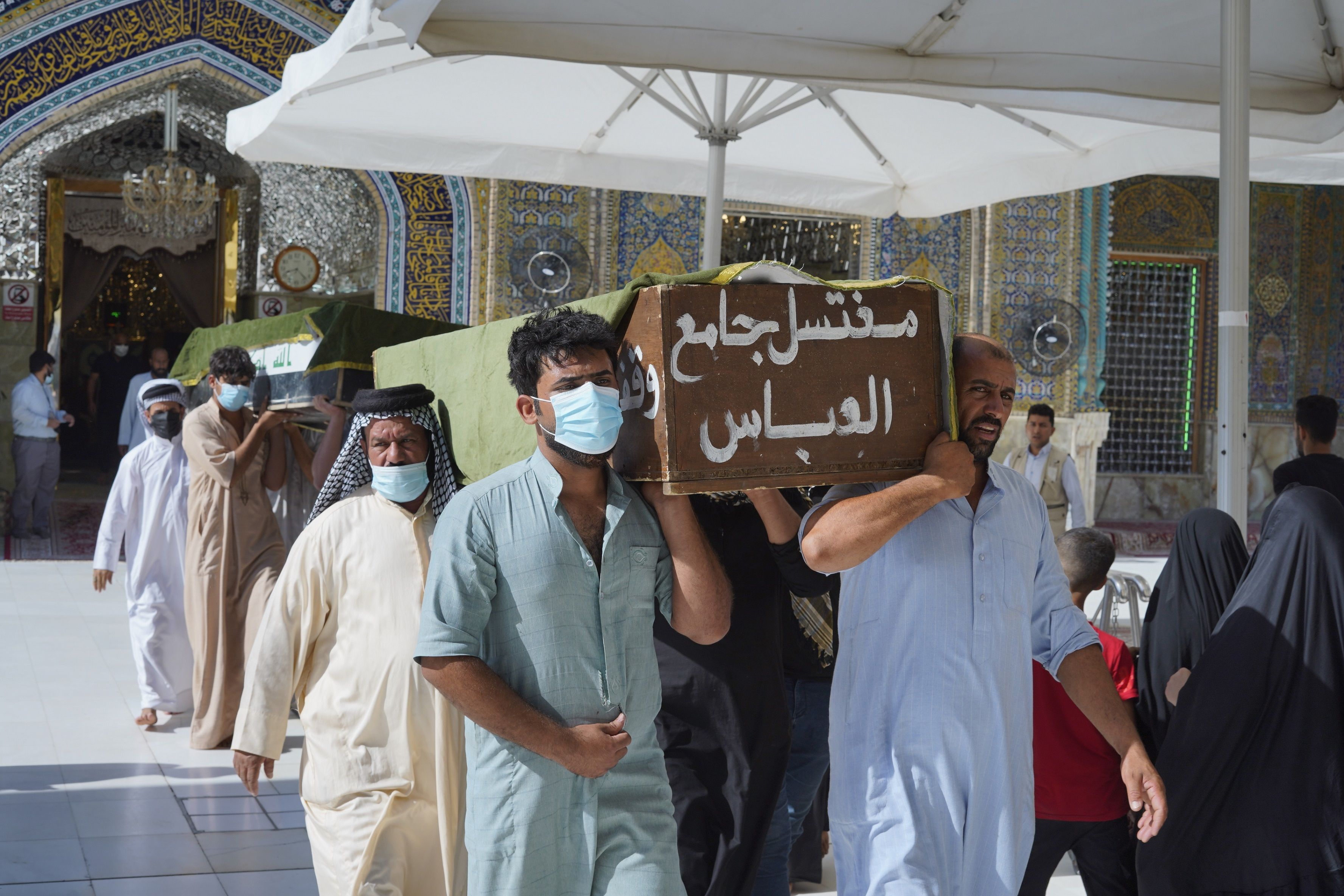 People at a funeral carry a coffin with an Arabic inscription