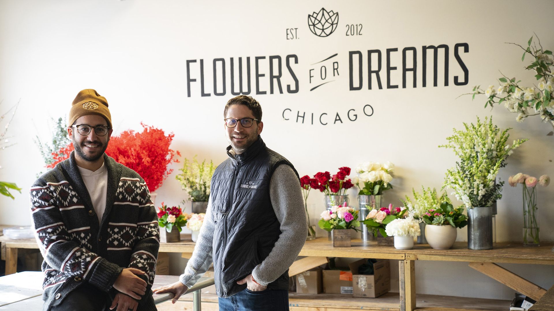 Photo of two men posing in front of flowers.