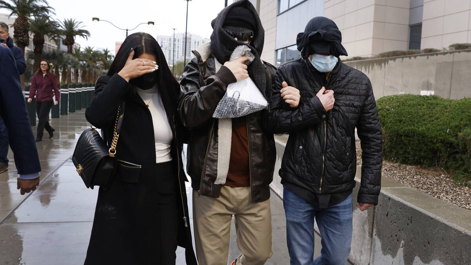 Three people walk down a sidewalk concealing their faces 