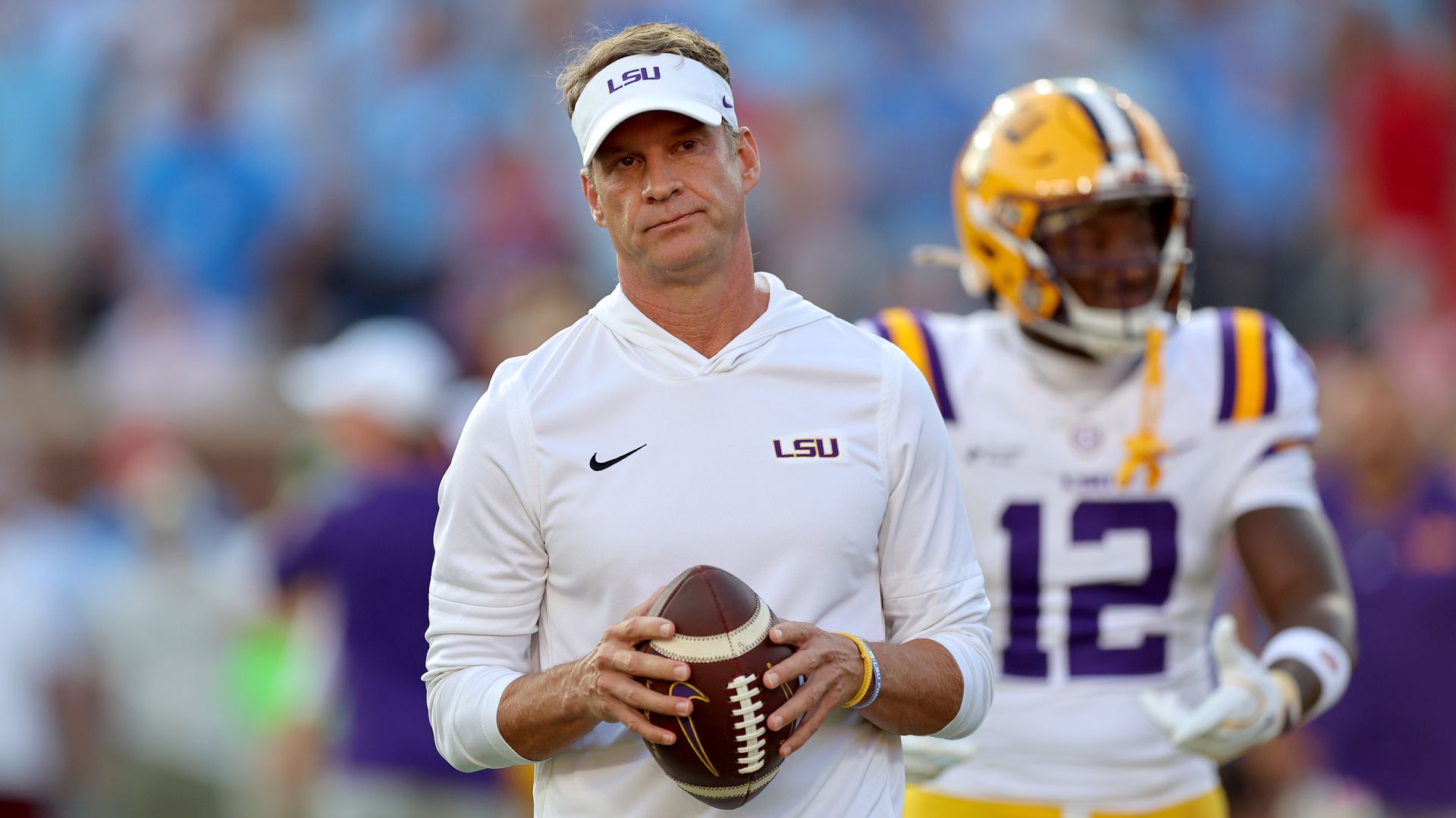 Lane Kiffin holds a football and looks sad.