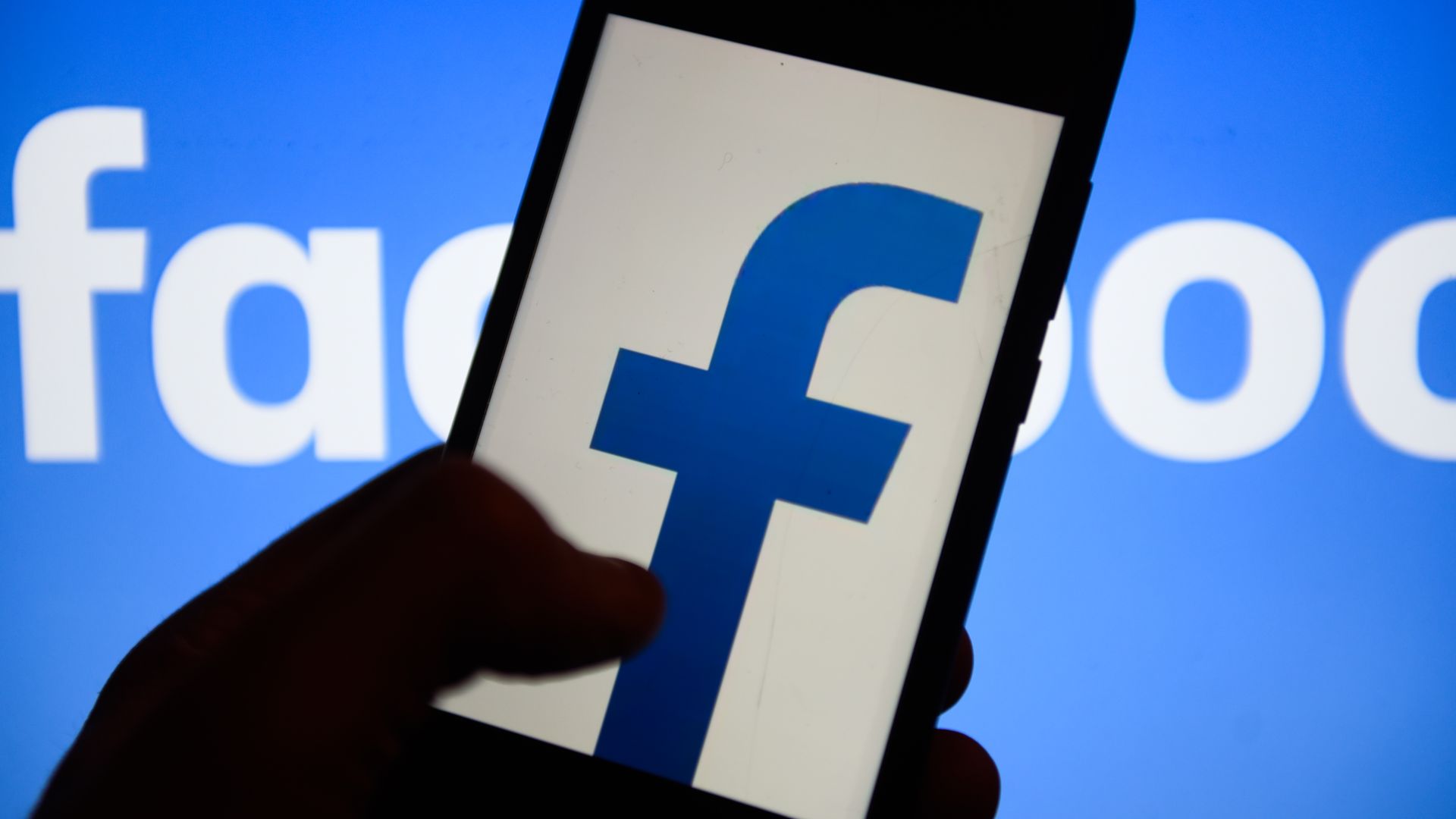 Facebook logo on smartphone screen with shadowy fingers