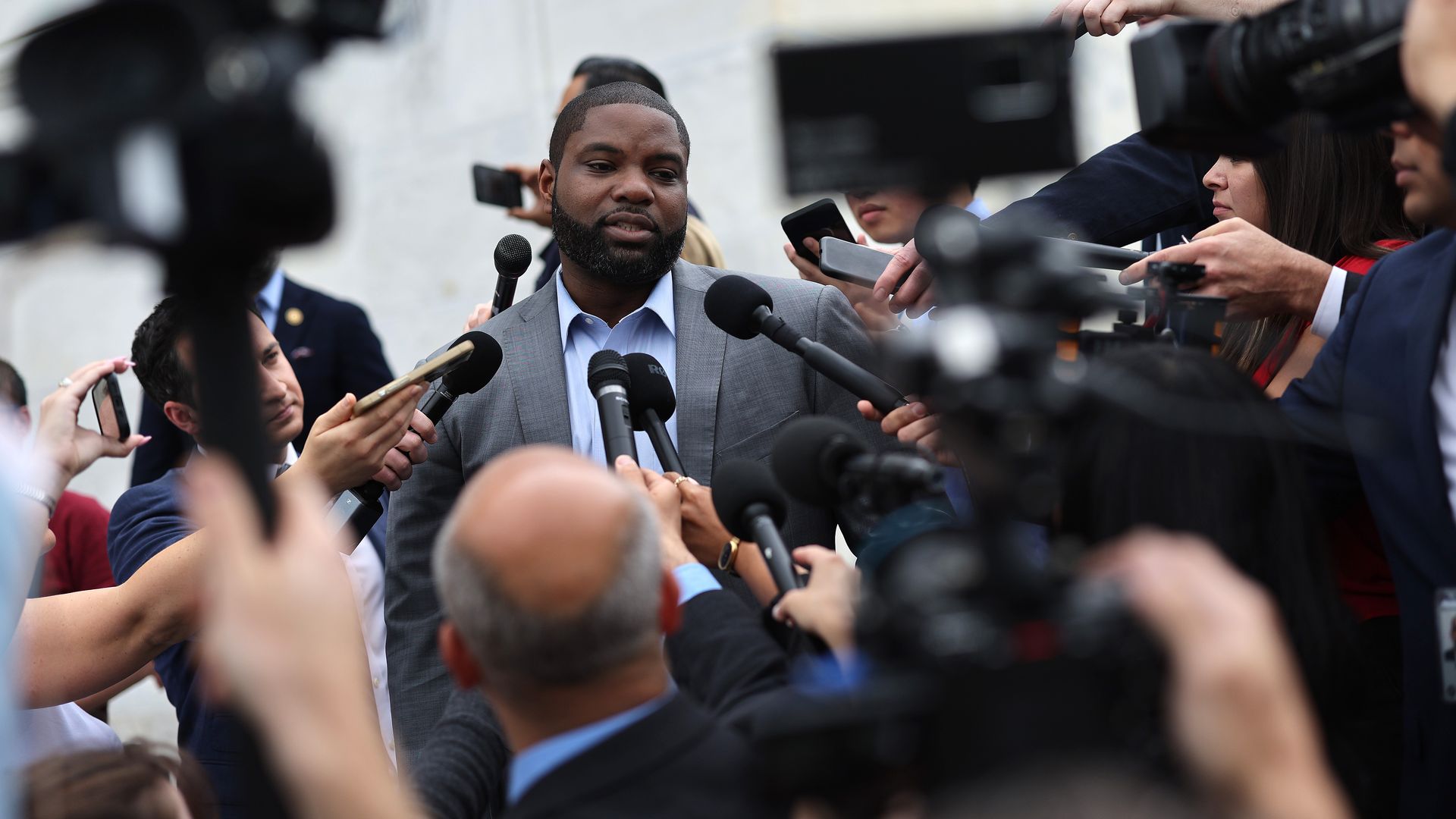 Rep. Byron Donalds, wearing a gray suit and speaking with reporters on the steps of the U.S. Capitol.
