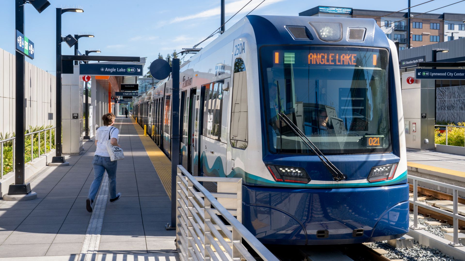 A person moves toward a Sound Transit train with "Angle Lake" written in glowing letters on the front of the train, next to a platform labeled "Shoreline." 