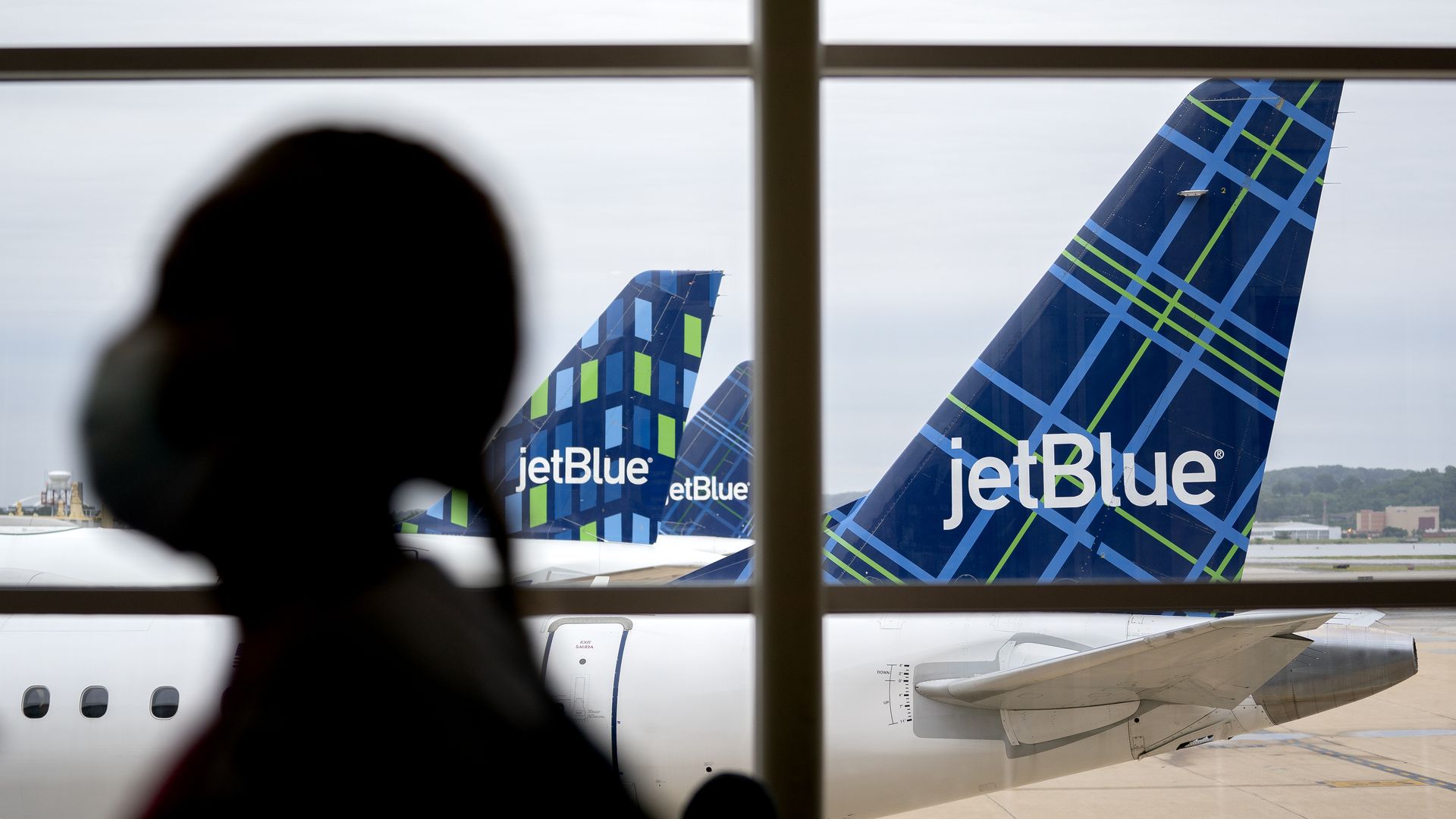 A traveler wearing a protective mask walks past JetBlue Airways Corp. aircraft at Ronald Reagan National Airport (DCA) in Arlington, Virginia, U.S., on Tuesday, May 25
