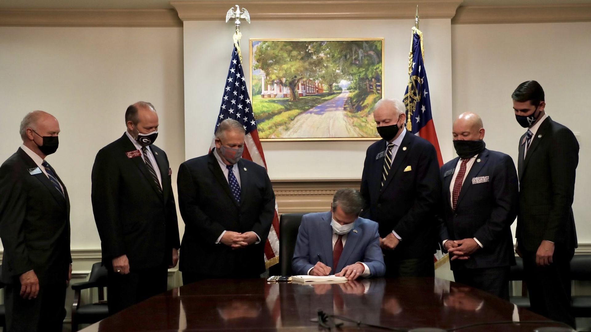 A photo of Brian Kemp signing the law with three men surrounding him at a table.