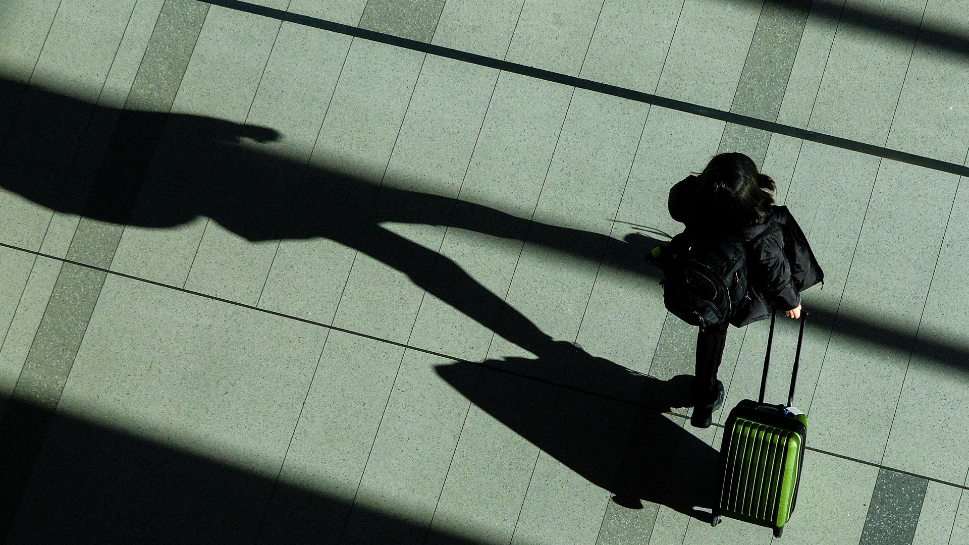 A passenger, seen from above and wearing all black, pulls a suitcase behind them in a terminal at LaGuardia airport.