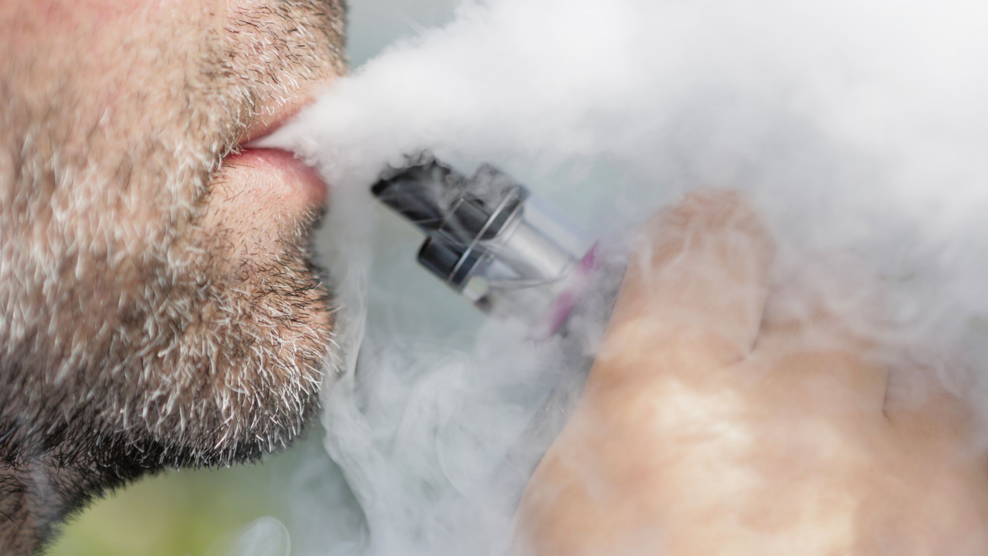 In this image, a man with a beard smokes with a vaping pen.