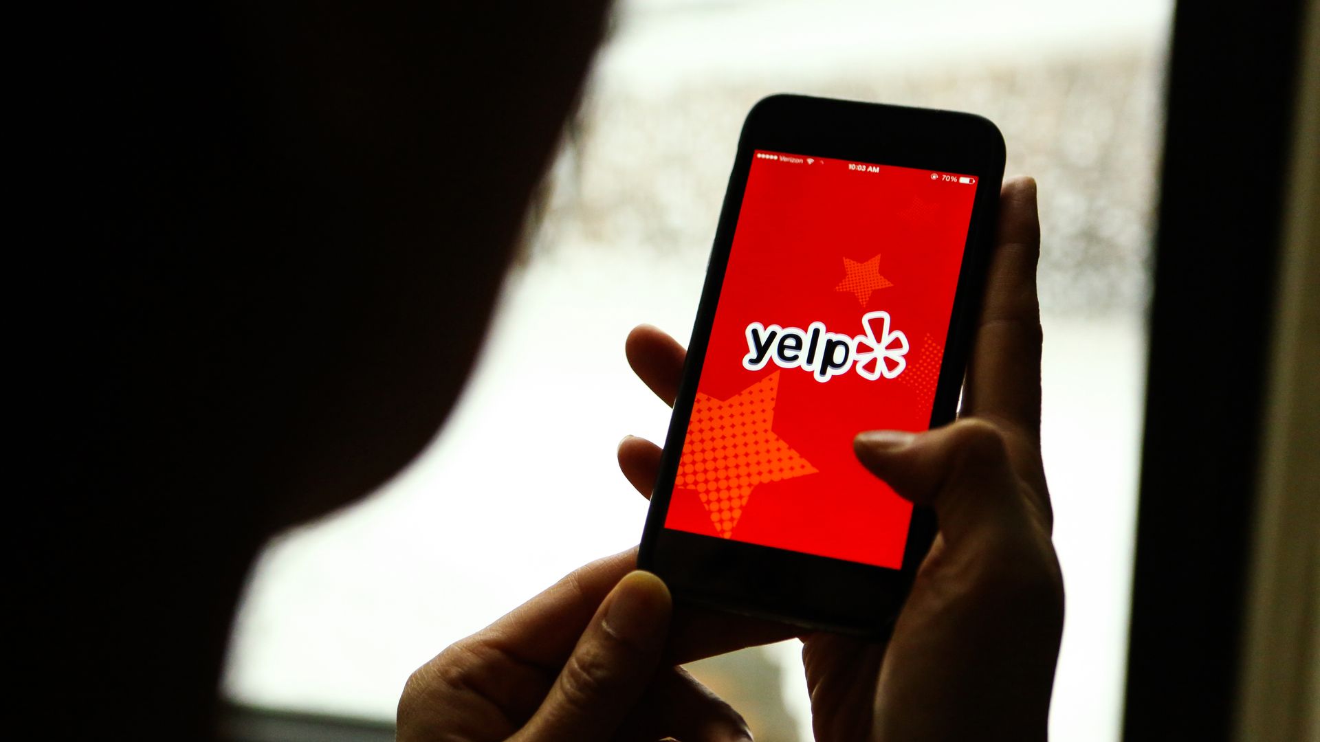 Picture of a person's hands holding a smartphone that has the Yelp logo on the screen