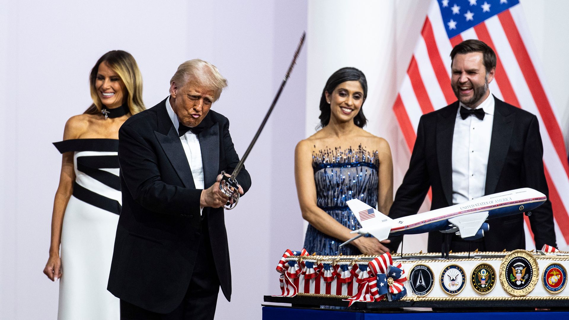 President Trump holds a sword while pursing his lips as Melania Trump, Usha Vance and JD Vance laugh beside him.