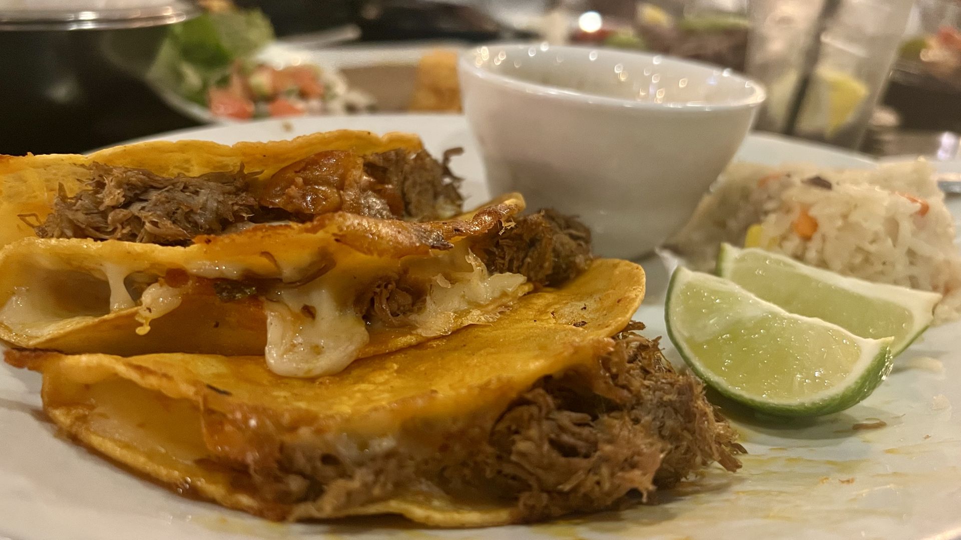 A plate with three tacos, two limes and rice