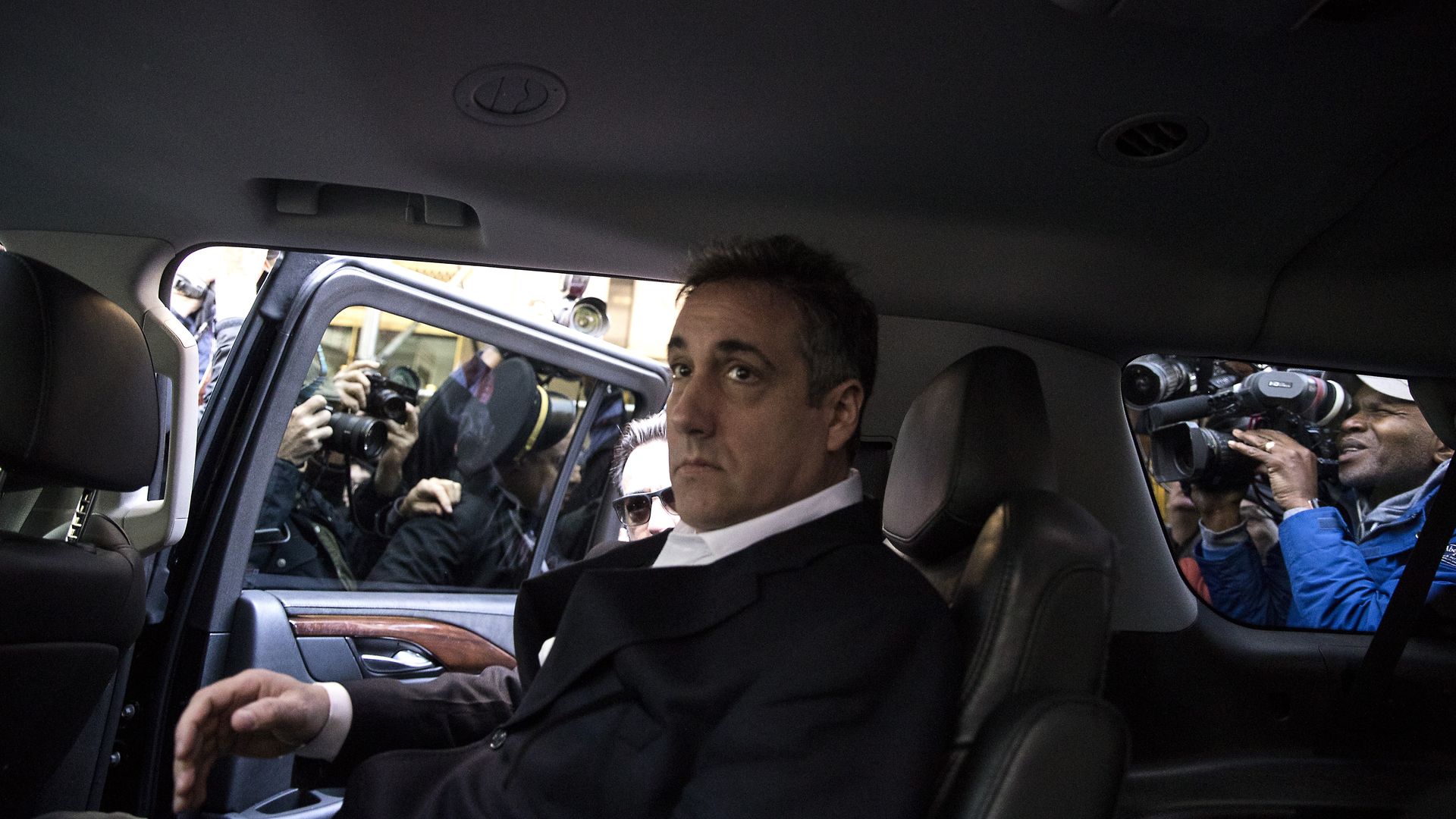 Photo of Michael Cohen sitting in a car with photographers surrounding him