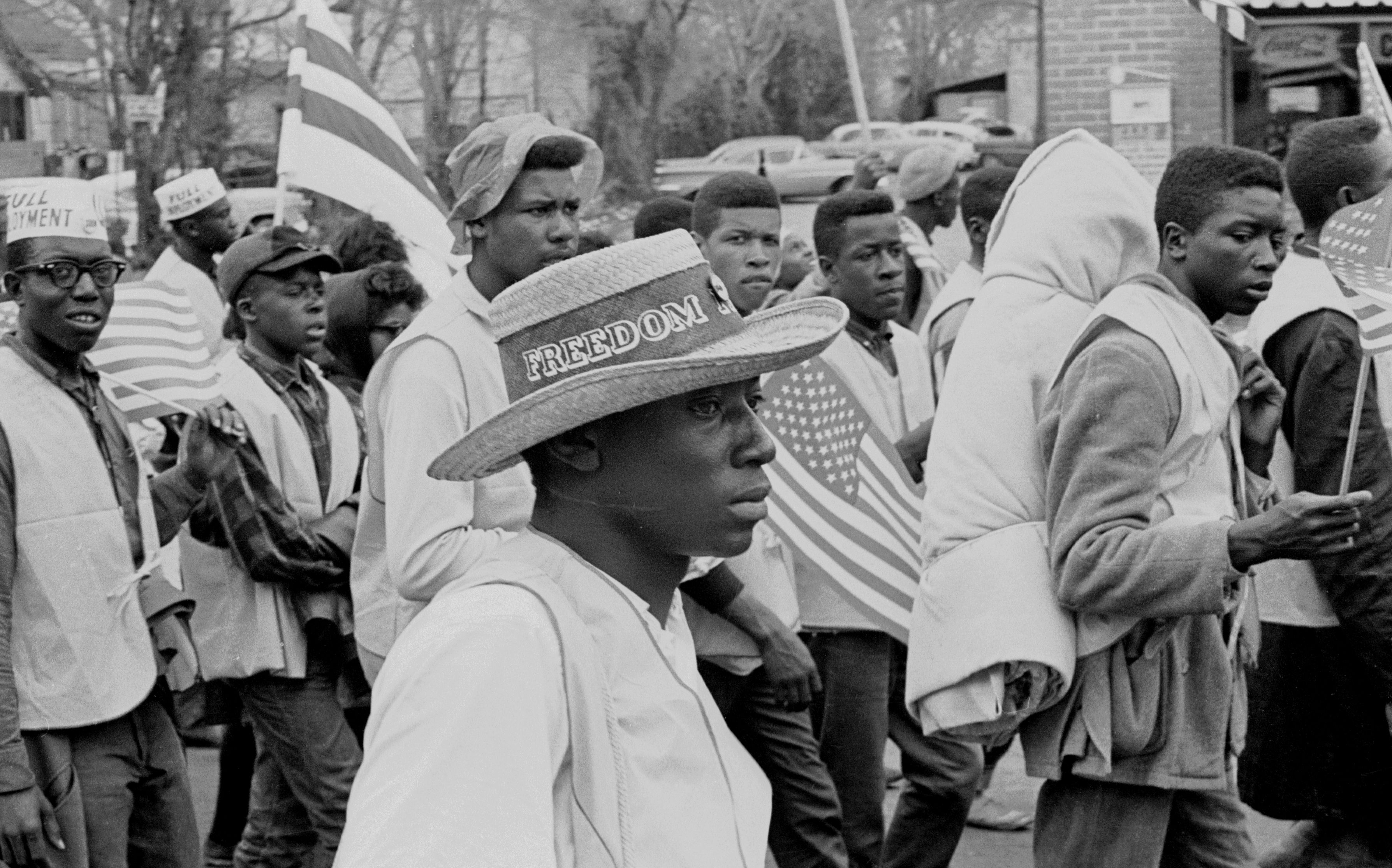 A man with a straw hat that reads 'Freedom' on its band walks with others during on the Selma to Montgomery marches held in support of voter rights, Alabama, late March, 1965