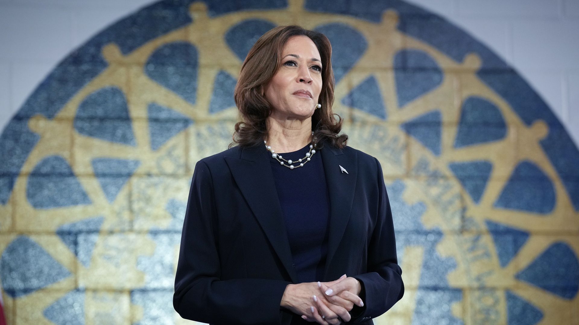 Kamala Harris standing in front of the seal of California in a black suit