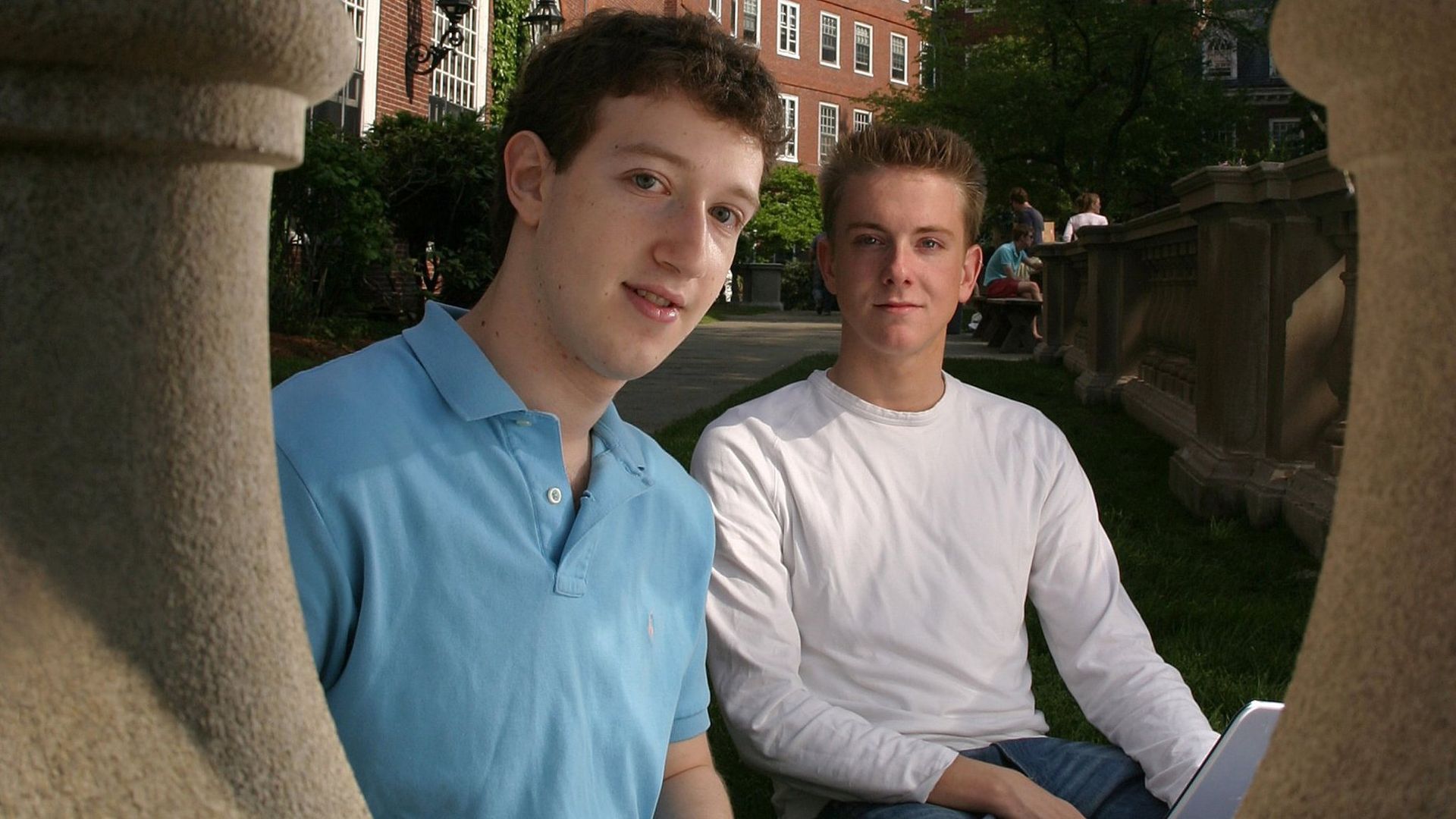 In this image, a young college aged Mark Zuckerberg sits in a polo shirt next to Chris Hughes.