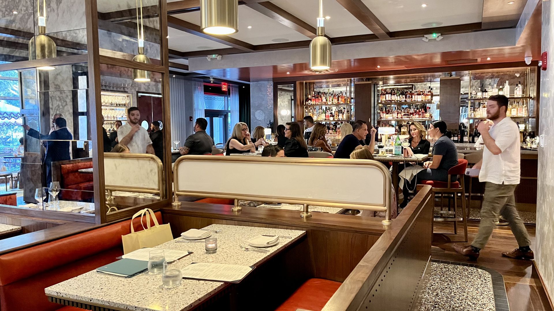 A view of an empty restaurant booth with red seats and a bar with glass shelves full of liquor bottles. 