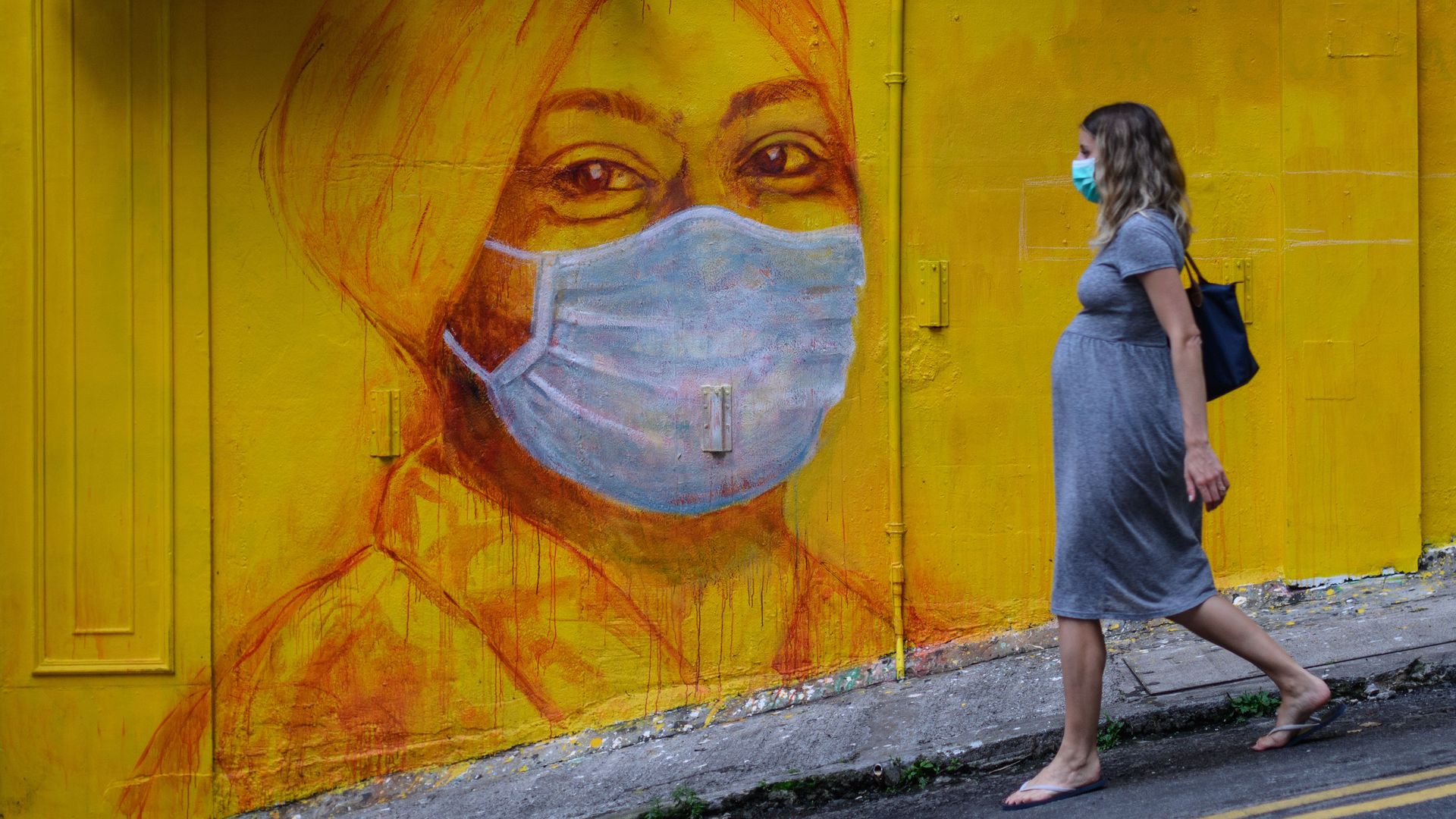 A pregnant woman wearing a face mask as a precautionary measure walks past a street mural in Hong Kong, on March 23, 2020,.
