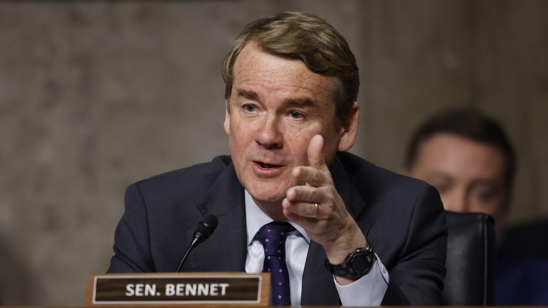 Senator Michael Bennet asks a question at a hearing, gesturing with his hand.