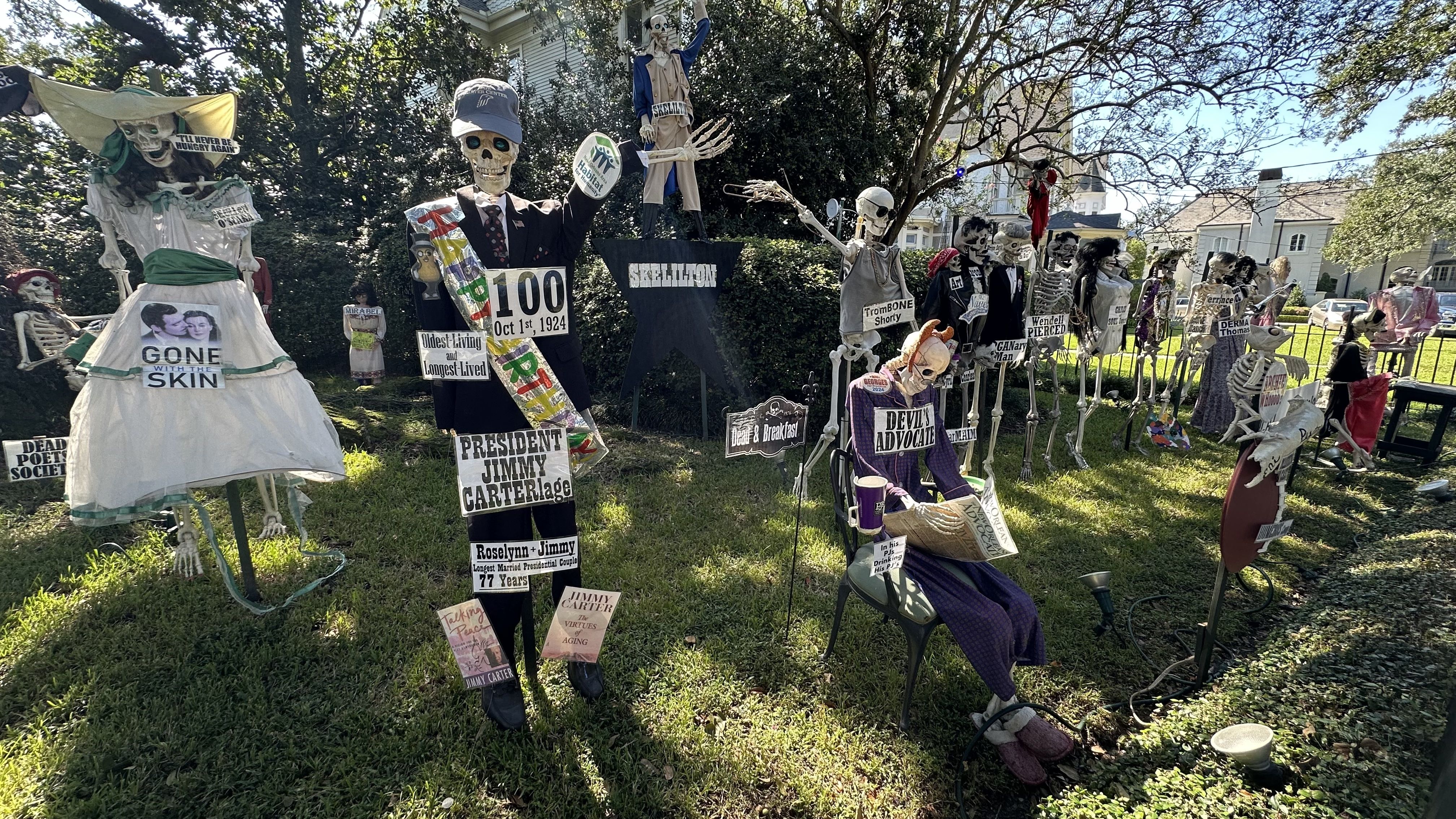 Skeletons decorate a yard and have signs with puns tied to Jimmy Carter and others.