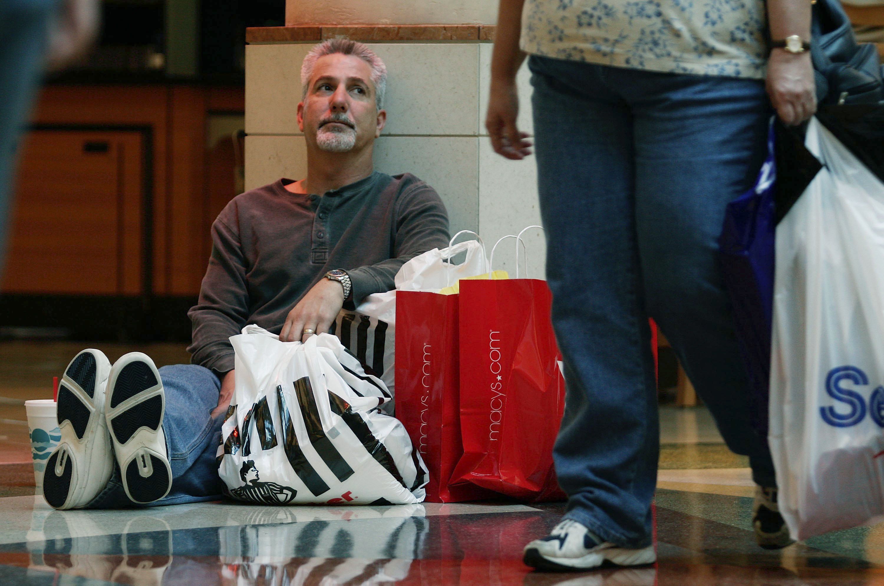 A man sitting on the floor surrounded by shopping bags. 