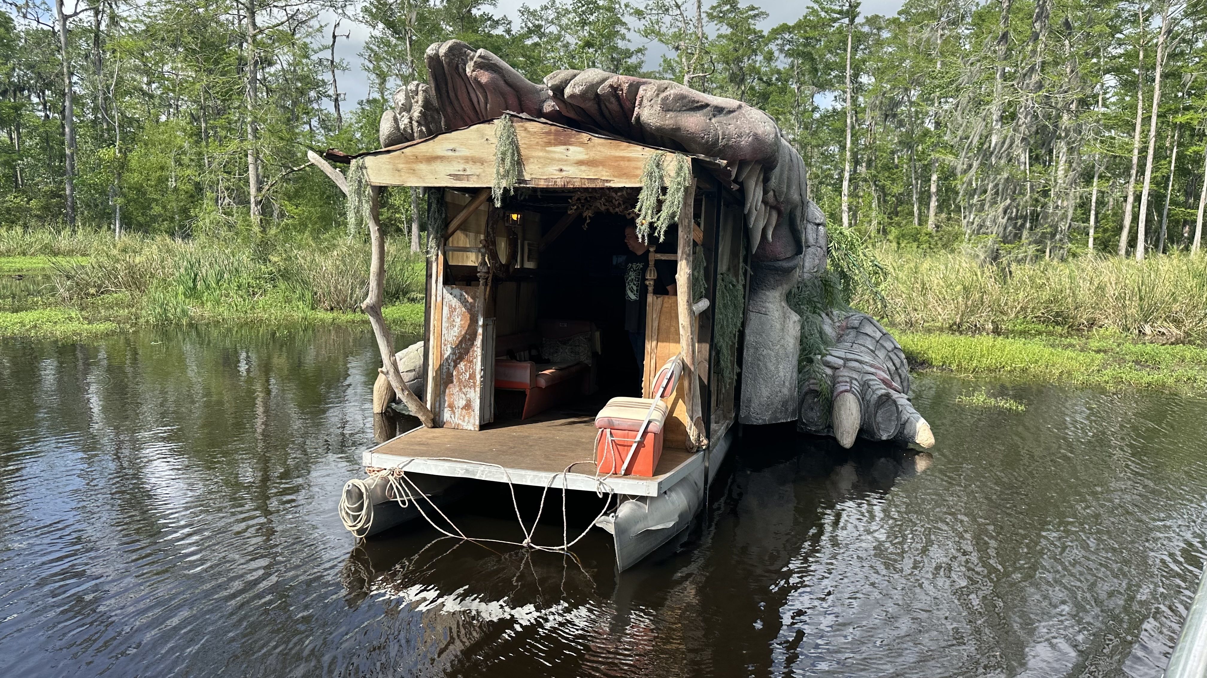 The front view of an alligator-shaped houseboat. The opening has a cooler aboard a pontoon.