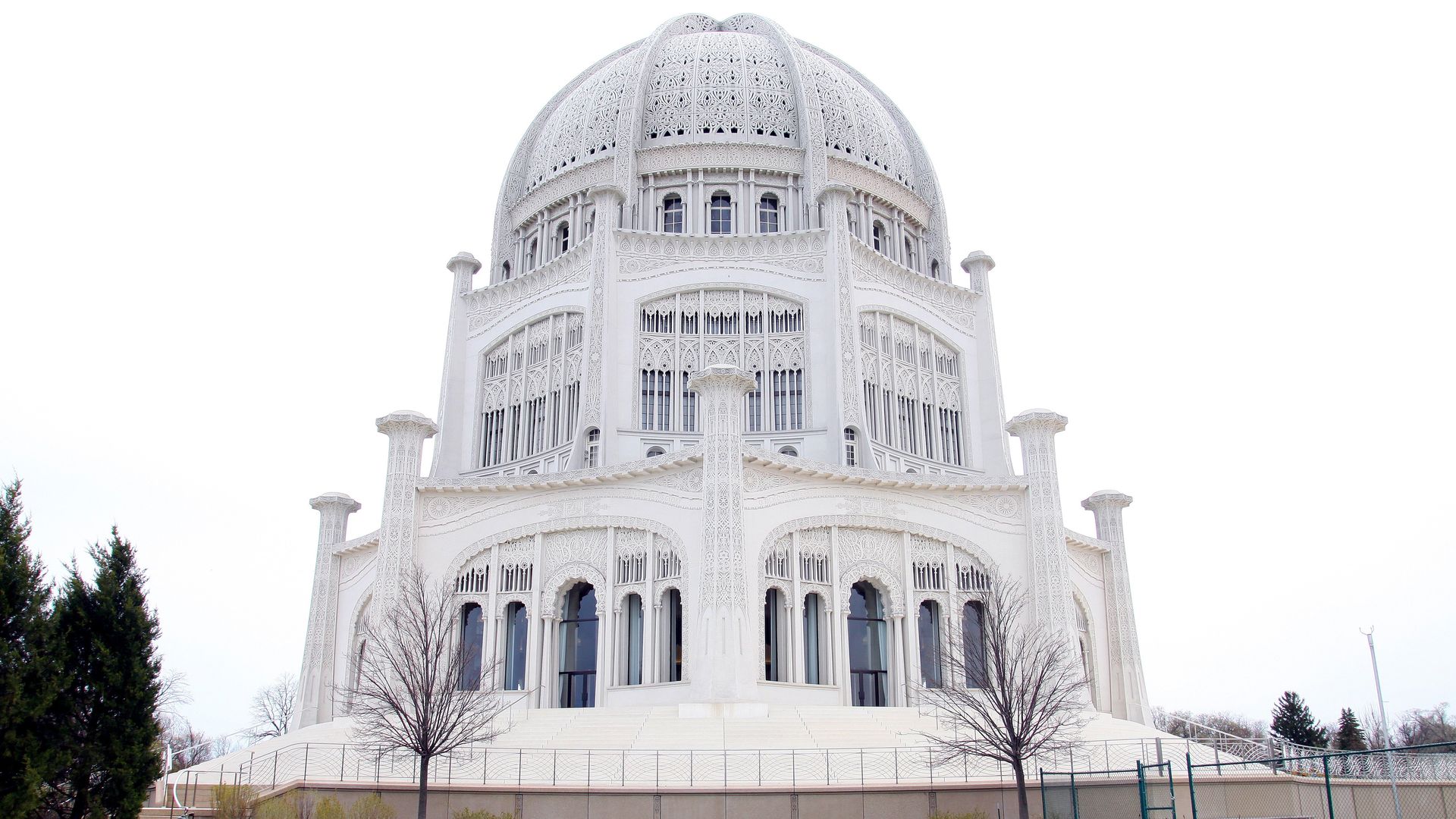 White ornate domed temple with intricate latticework and arched windows. Foreground features a circular fountain, manicured lawn, and vibrant orange tulip beds.