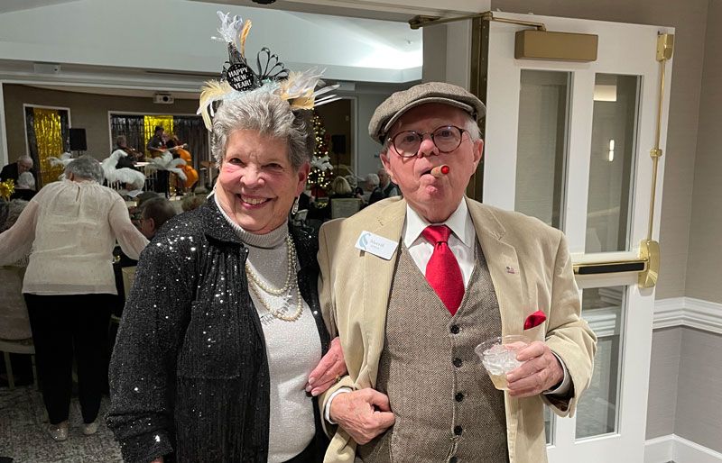 A cheerful senior couple dressed for a festive celebration, smiling and posing happily together indoors.