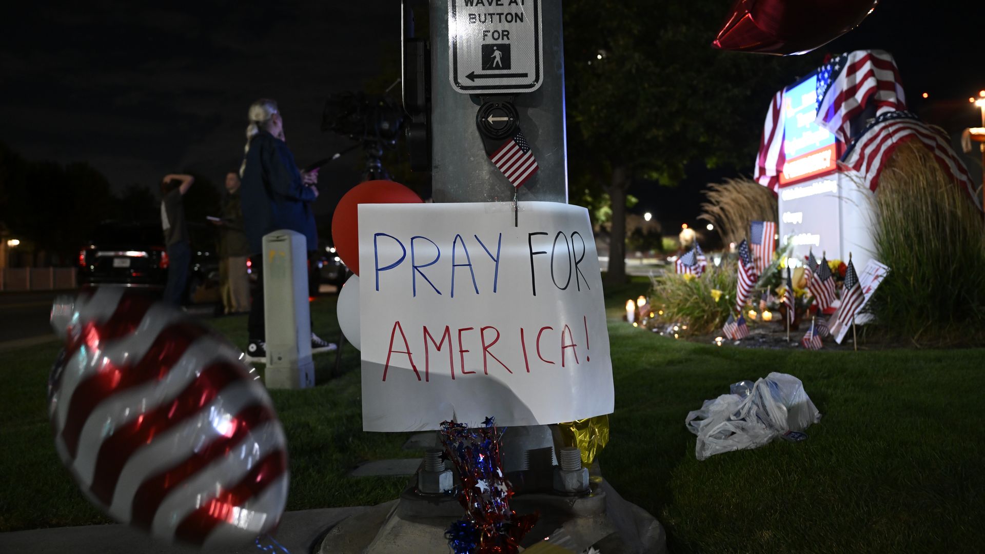 A sign reading "Pray For America" among American flags near a makeshift memorial outside a hospital