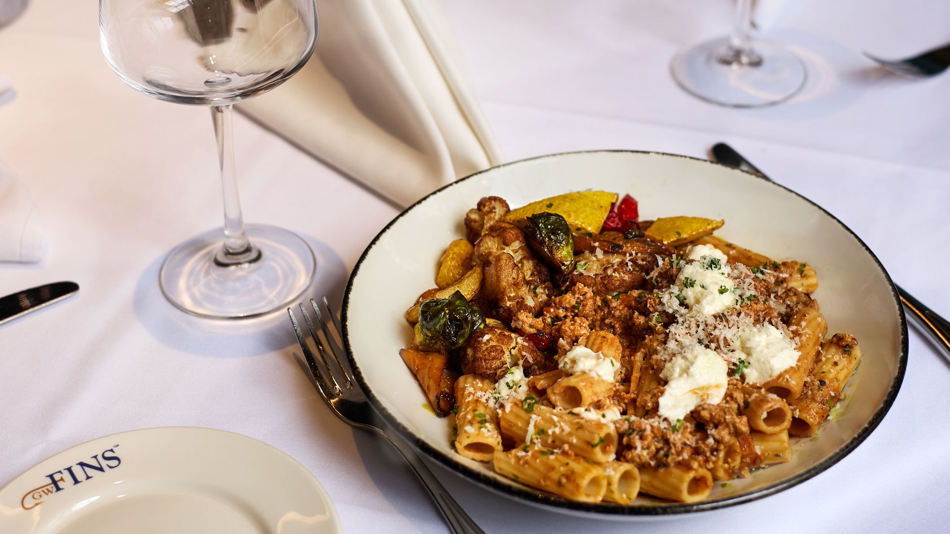 Image shows a plate of food with a wine glass at GW Fins