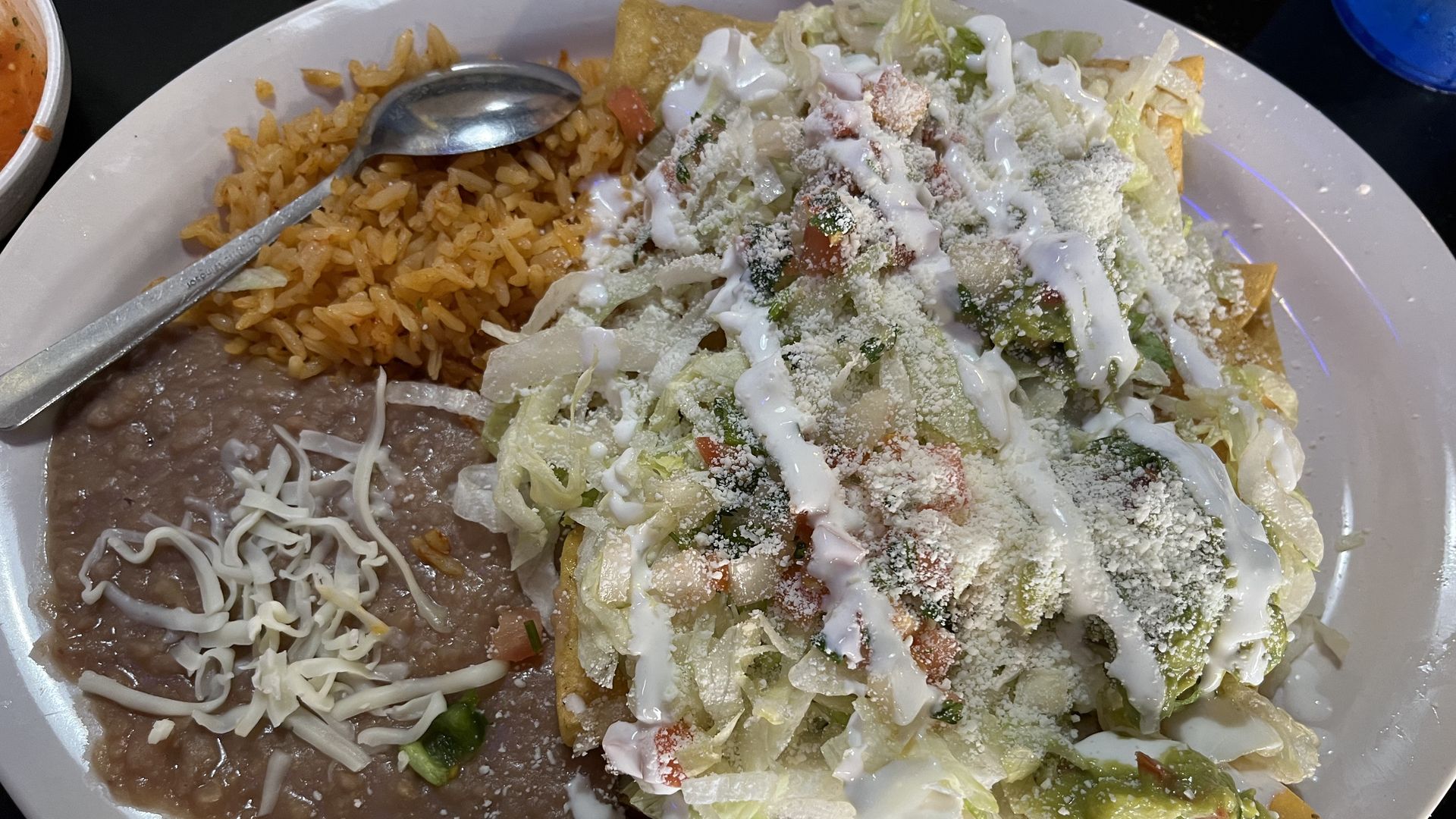 Plate filled with beans, rice and a taquito with lettuce and sauce drizzled on top.