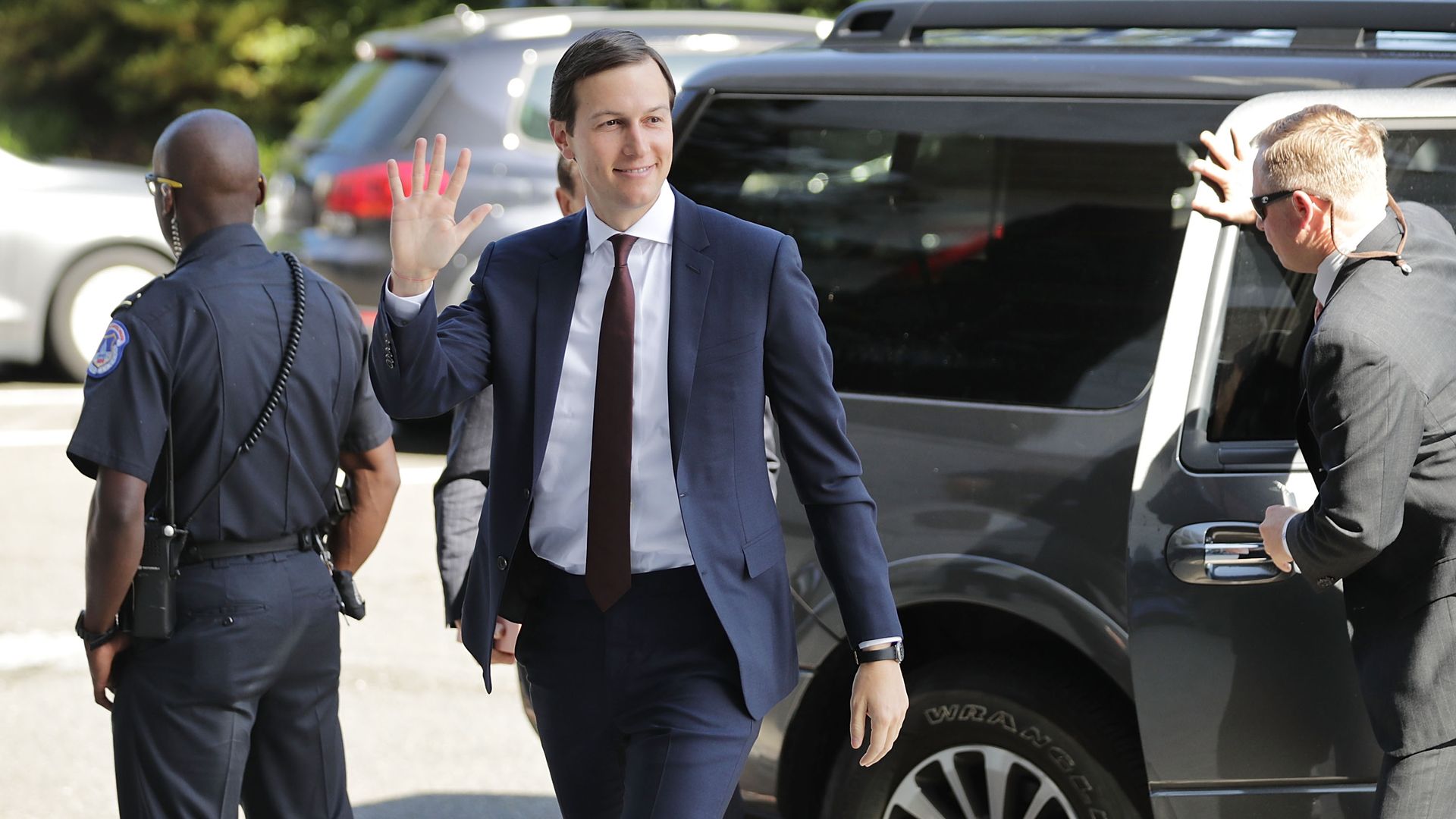 Jared Kushner in a dark grey suit waving as he walks away from a car