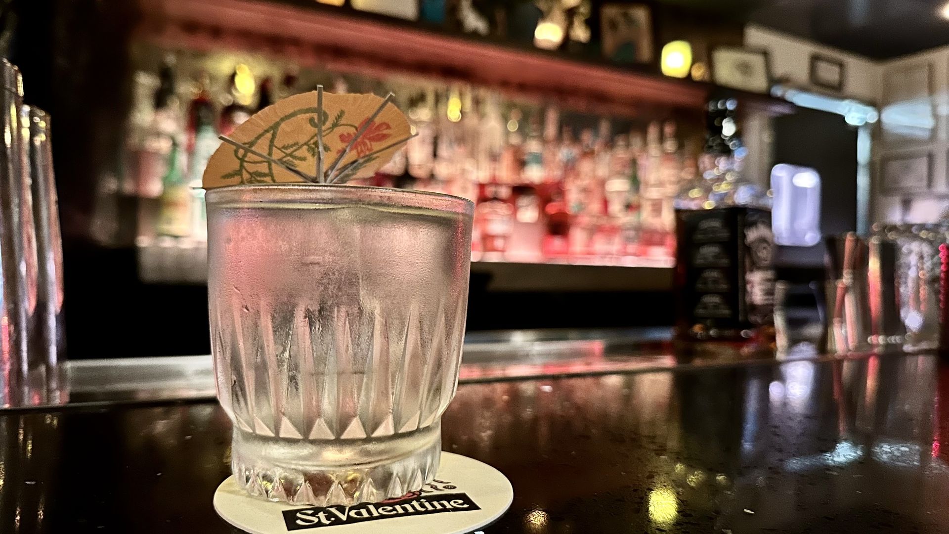 A clear mai-tai with an umbrella in the drink on a bar