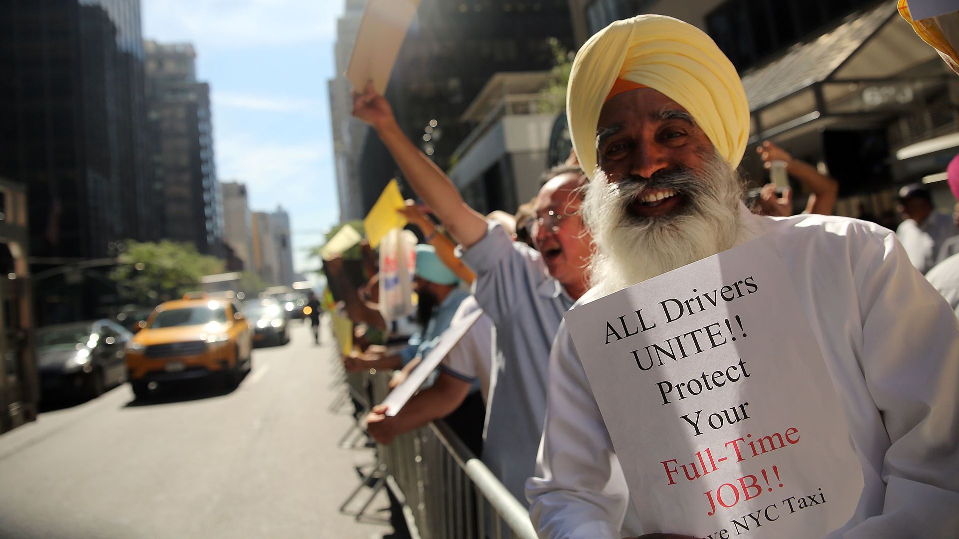 NYC taxi drivers protesting. One holds a sign: "ALL DRIVERS UNITE!! Protect your Full-Time JOB!"