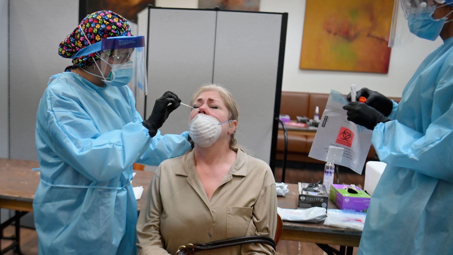 In this image, a woman is given a nasal swab by a health care worker