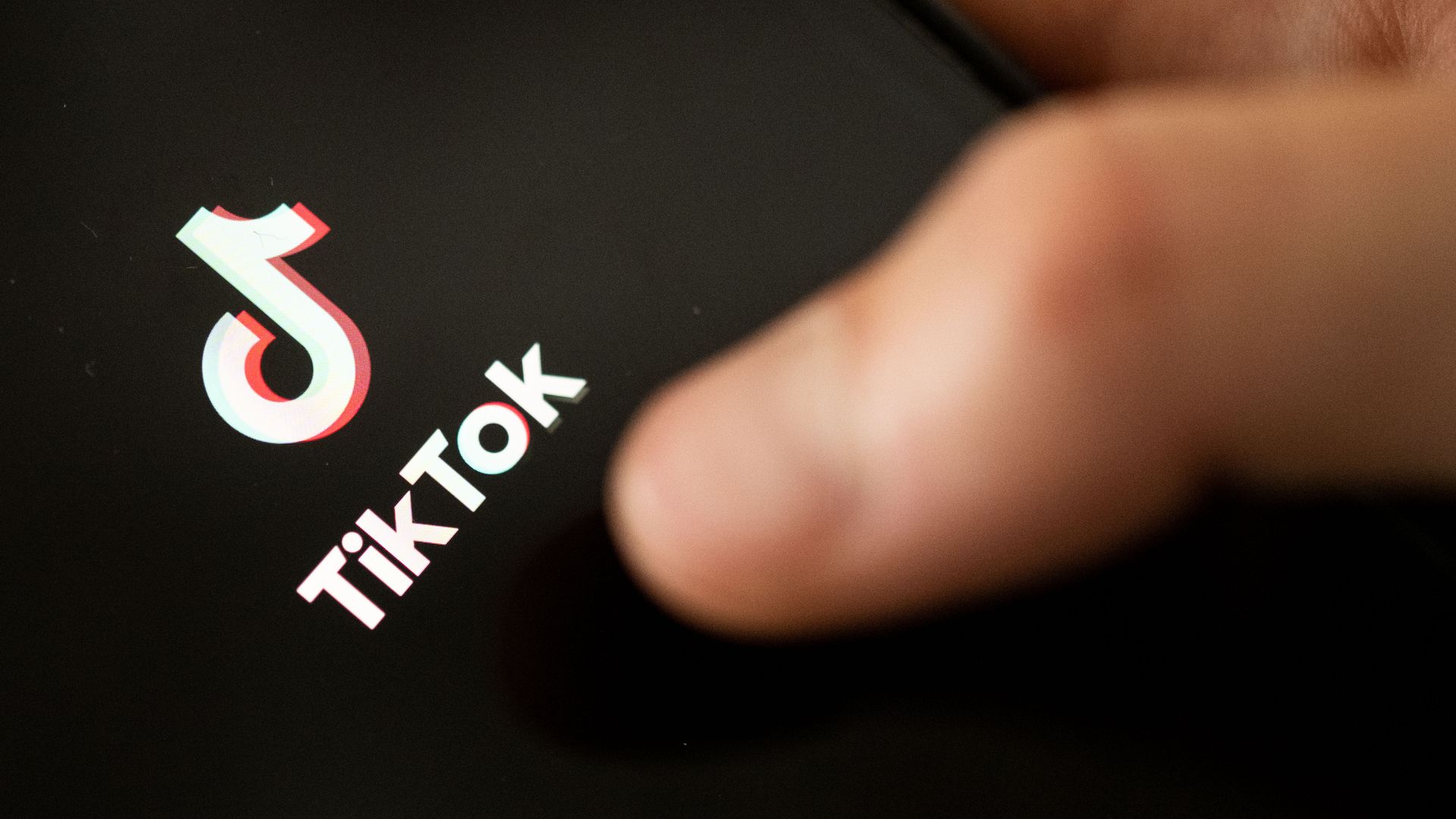 Photo of a thumb clicking on the TikTok app logo as shown on a phone screen