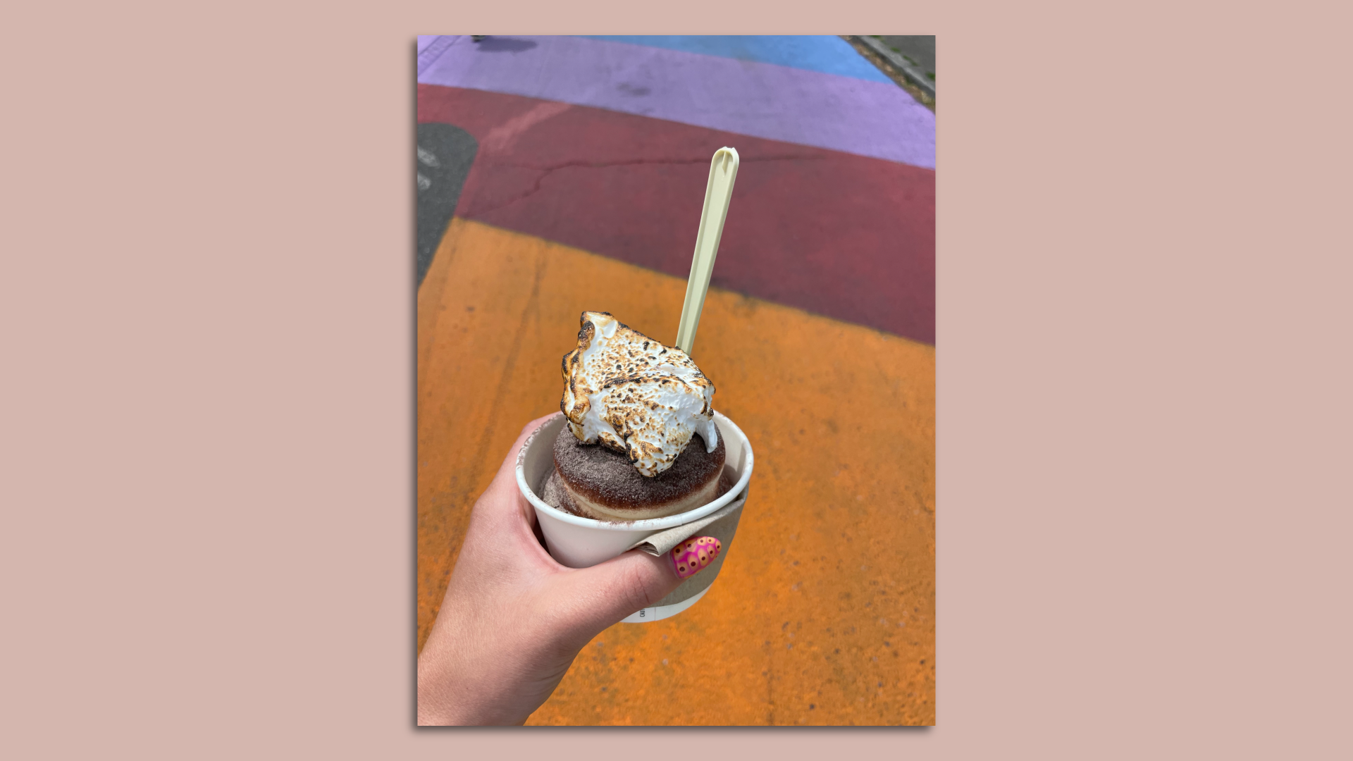 An image of a person holding a cup of soft serve ice cream with a spoon sticking out of it.