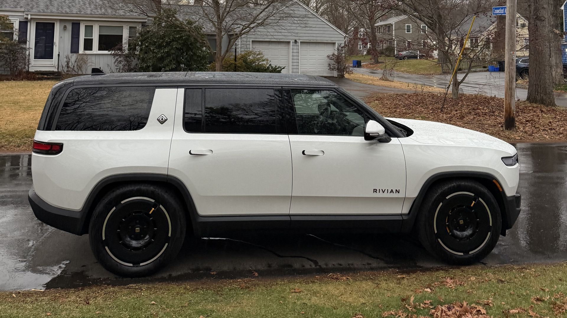 A white Rivian R1S is parked on a suburban street.