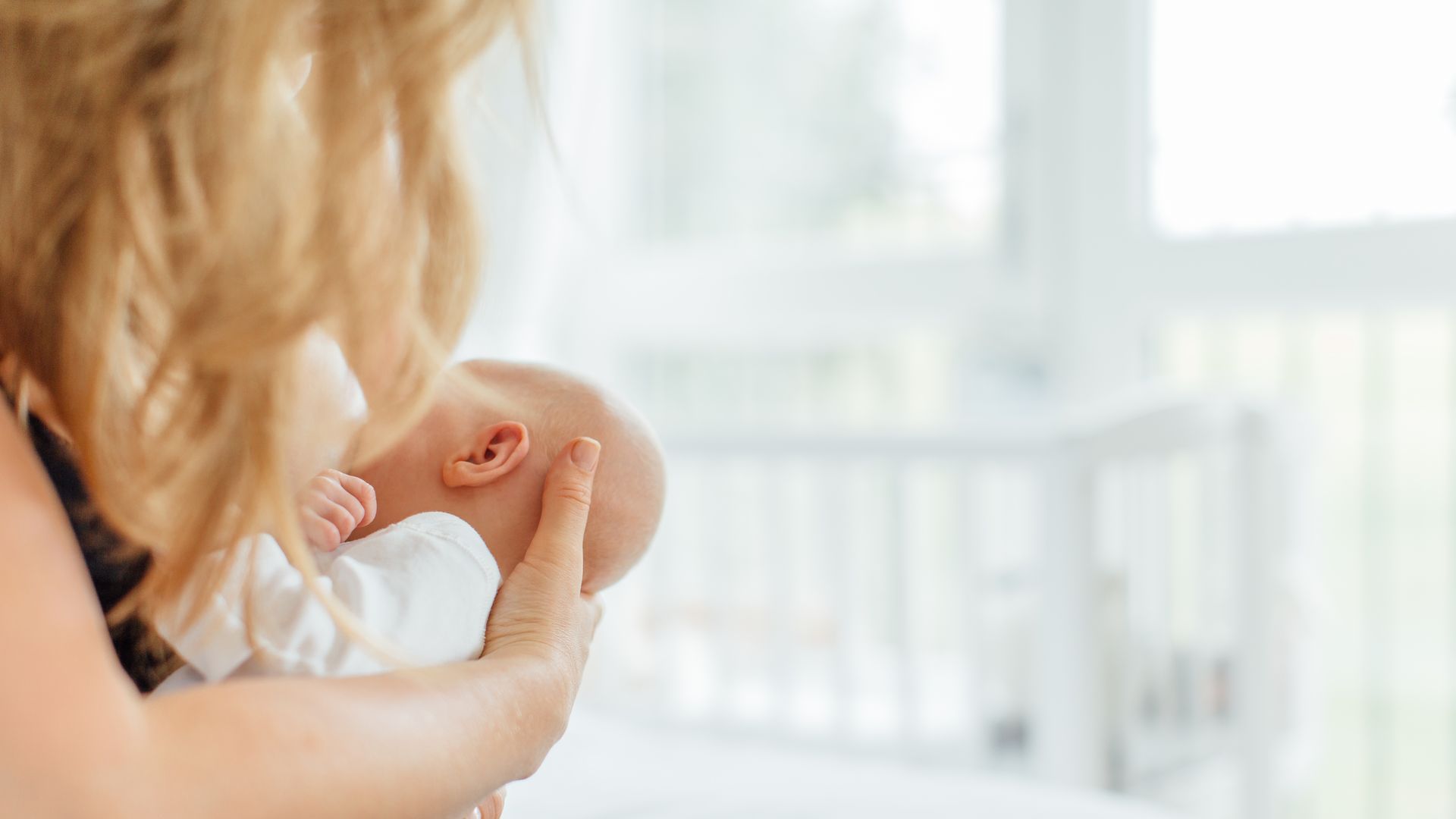 In this image, a blonde woman holds a swaddled infant to her chest.