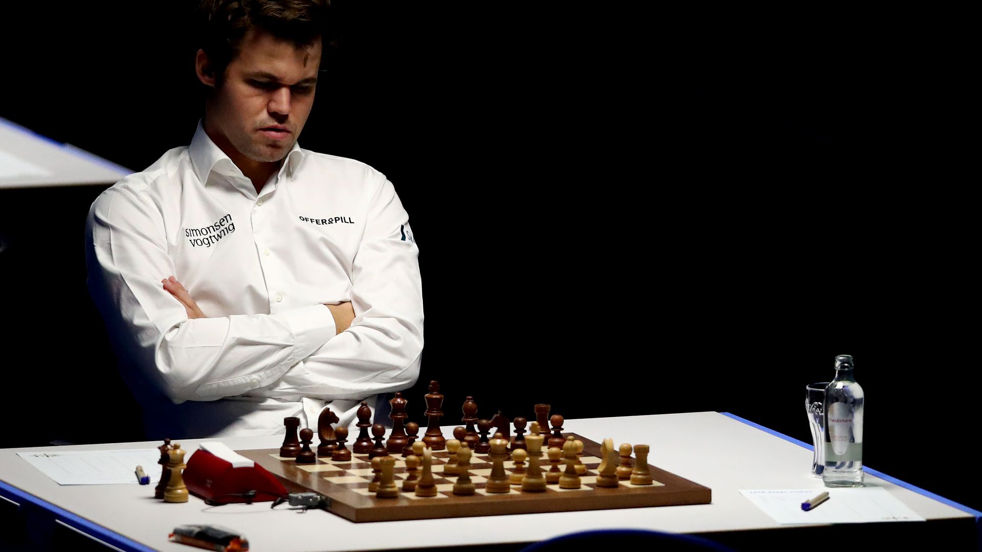 Chess champion Magnus Carlsen folds his arms across his chess as he contemplates his next move.
