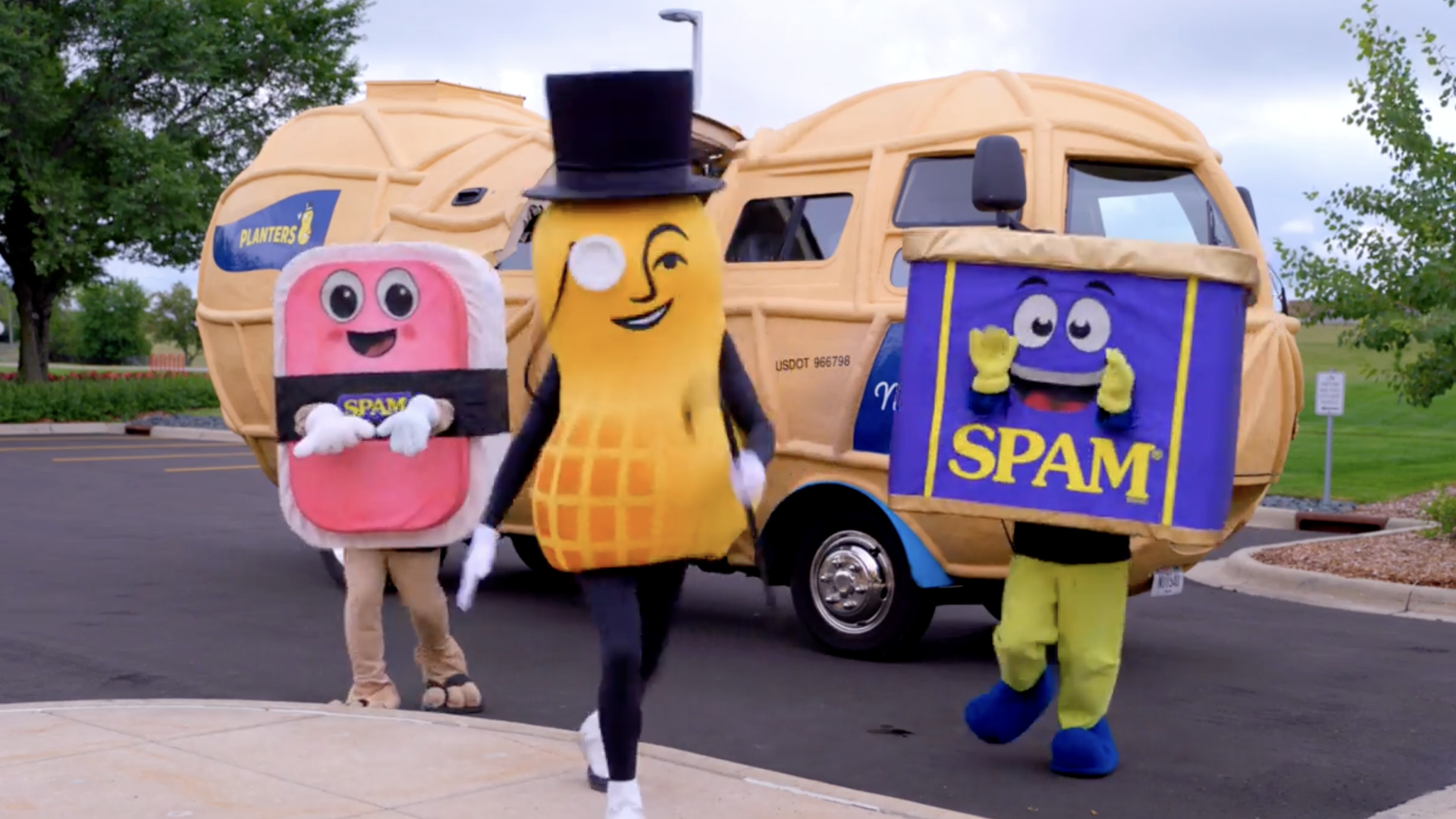 Mr. Peanut dances with two Spam can mascots outside of a peanut truck 