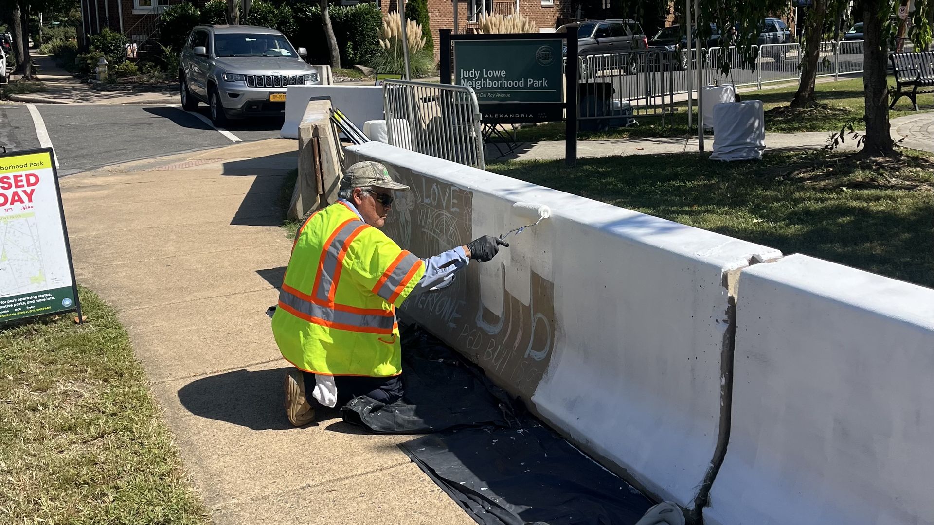A photo of a man painting over chalk graffiti on a concrete barricade.