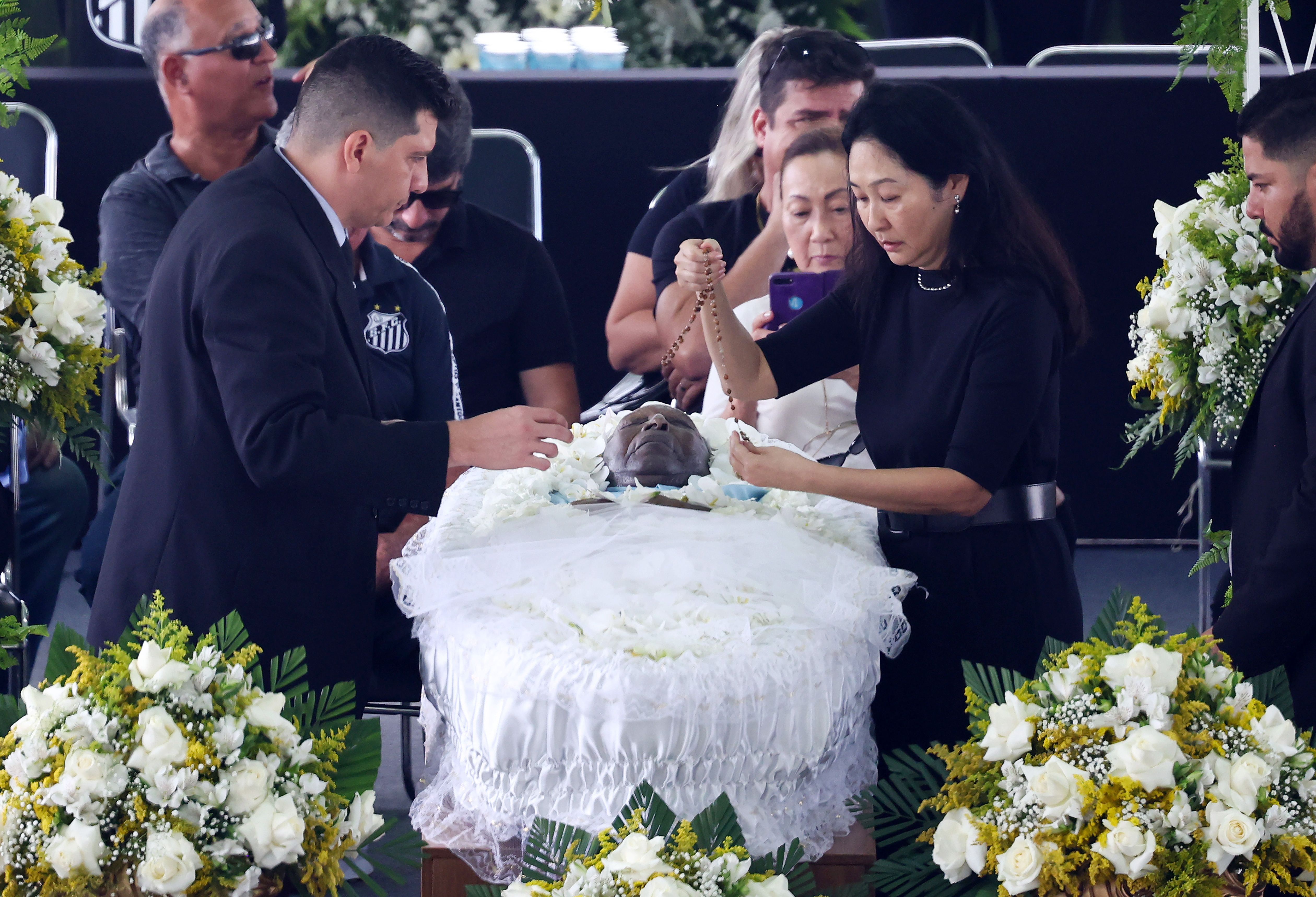 Pele's wife Marcia Aoki (2nd R) places a rosary on Pele's coffin in Urbano Caldeira Stadium at his funeral on January 02, 2023 in Santos, Brazil.