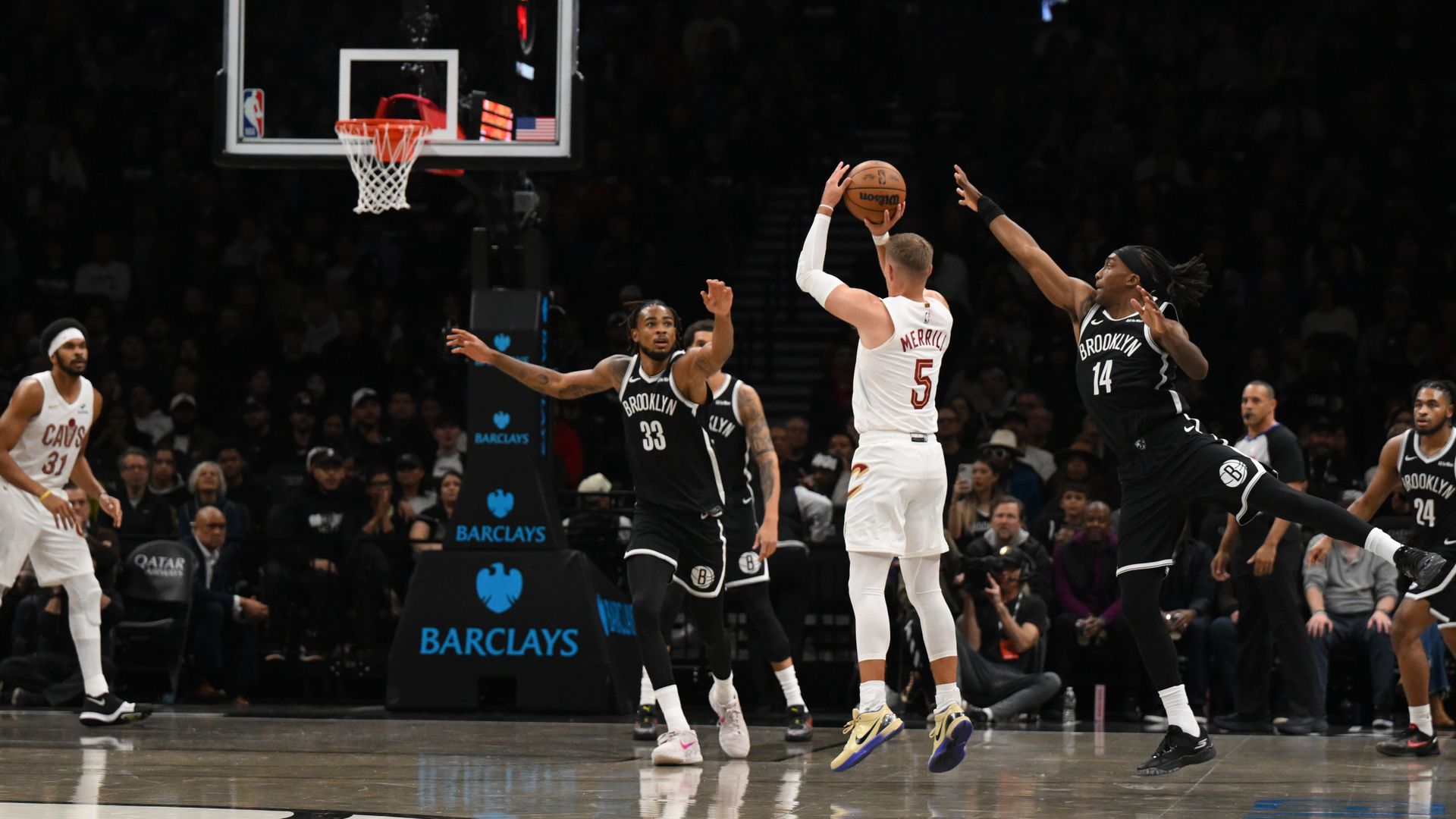 Man in white jersey shoots basketball, defended by men in black jerseys