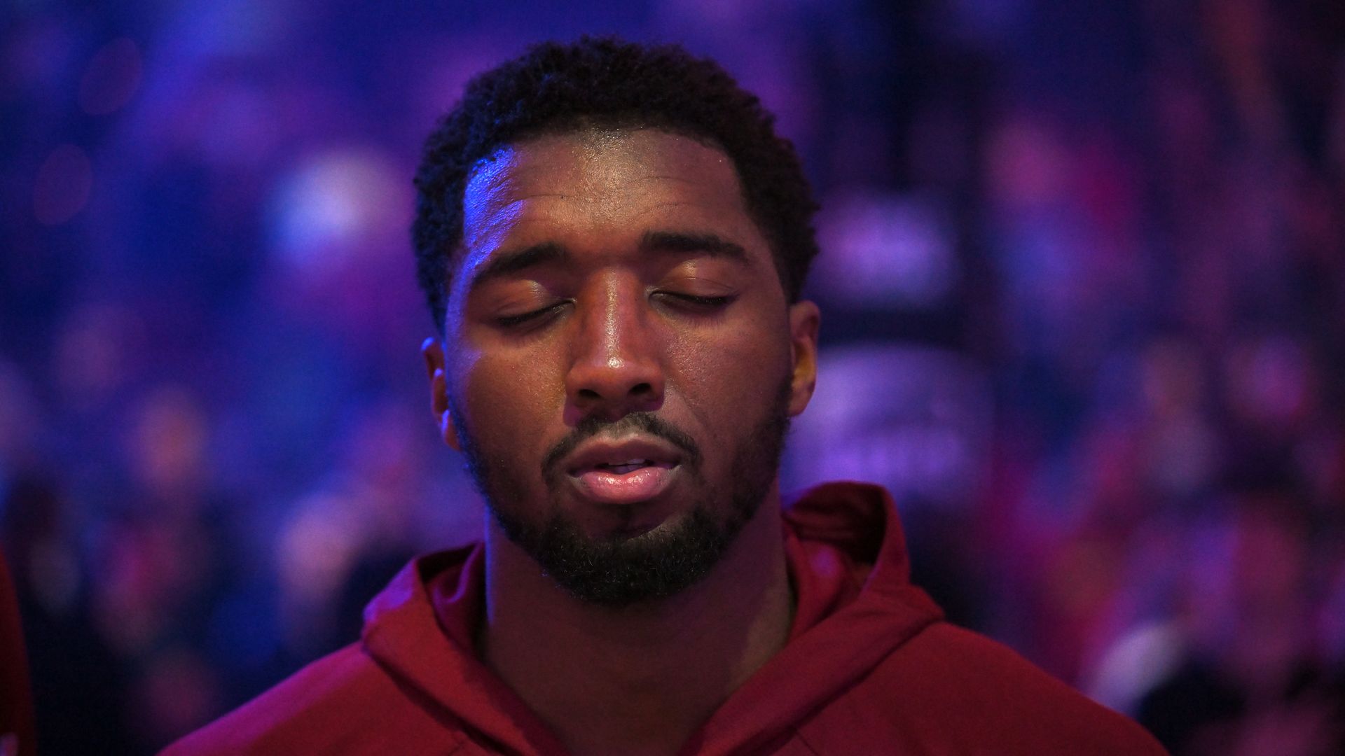 Sweaty black man in red warmup jacket with eyes closed.