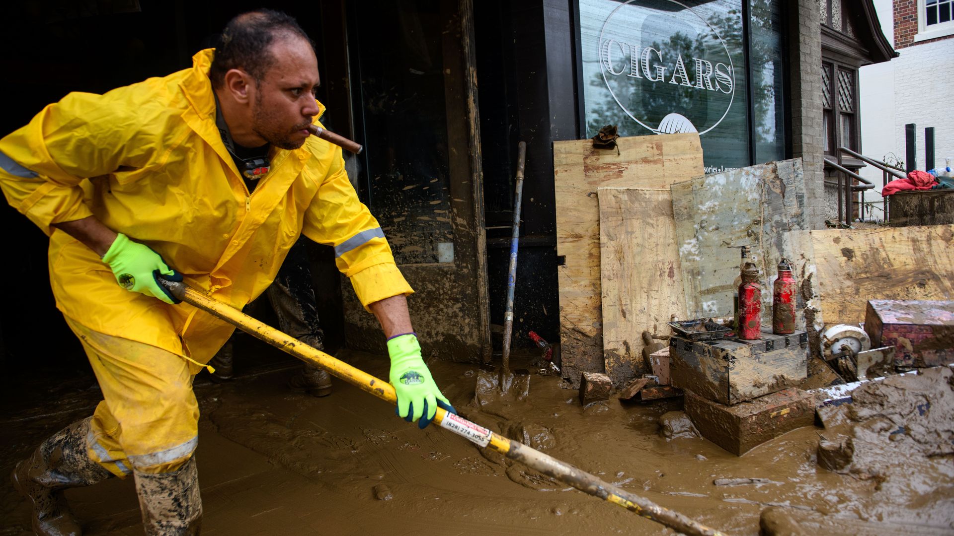 A man in a yellow rain slicker pushes mud out of a cigar store after a severe flood.