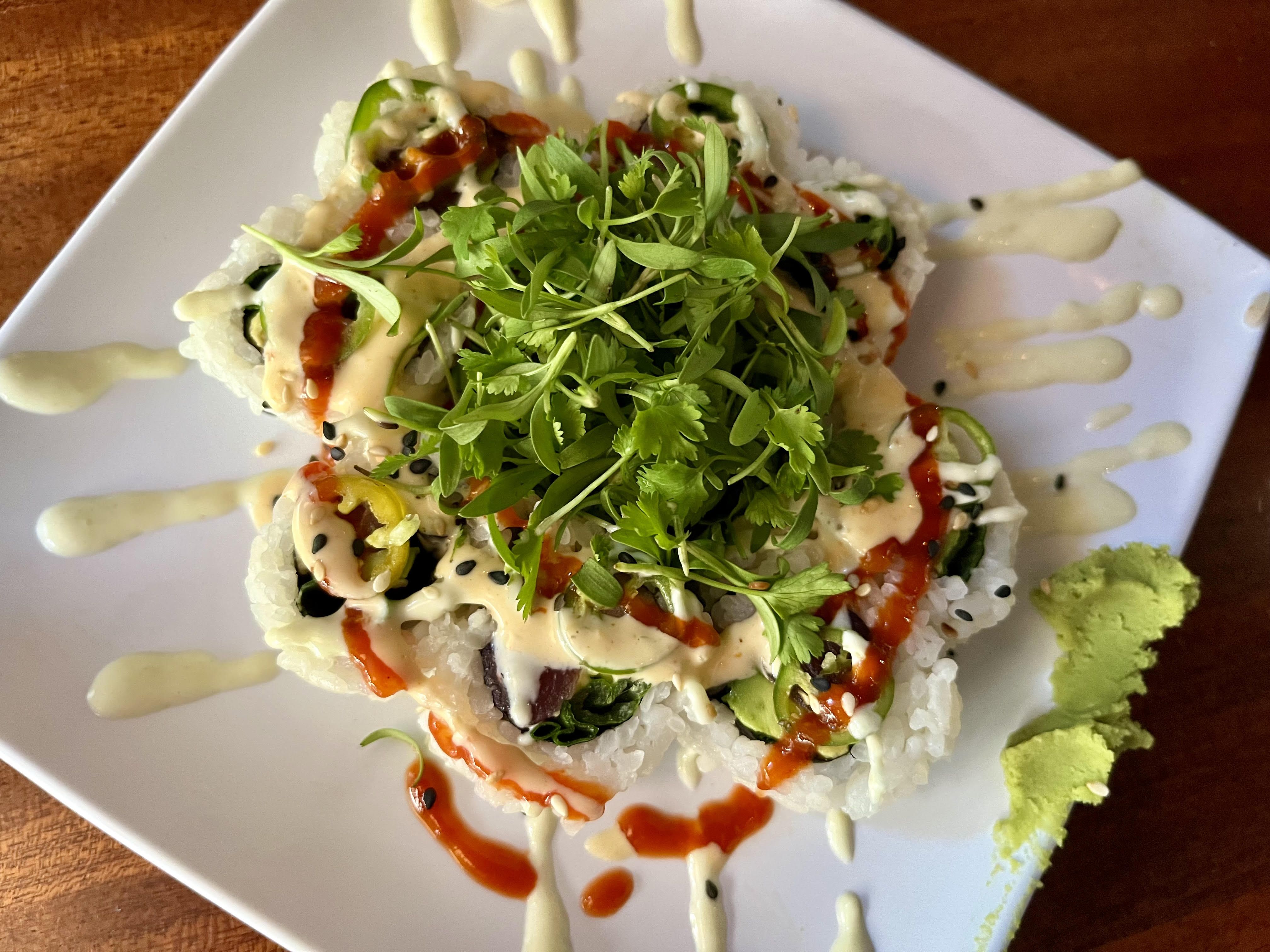 A sushi roll with decorative sauce around it and a pile of cilantro on top.