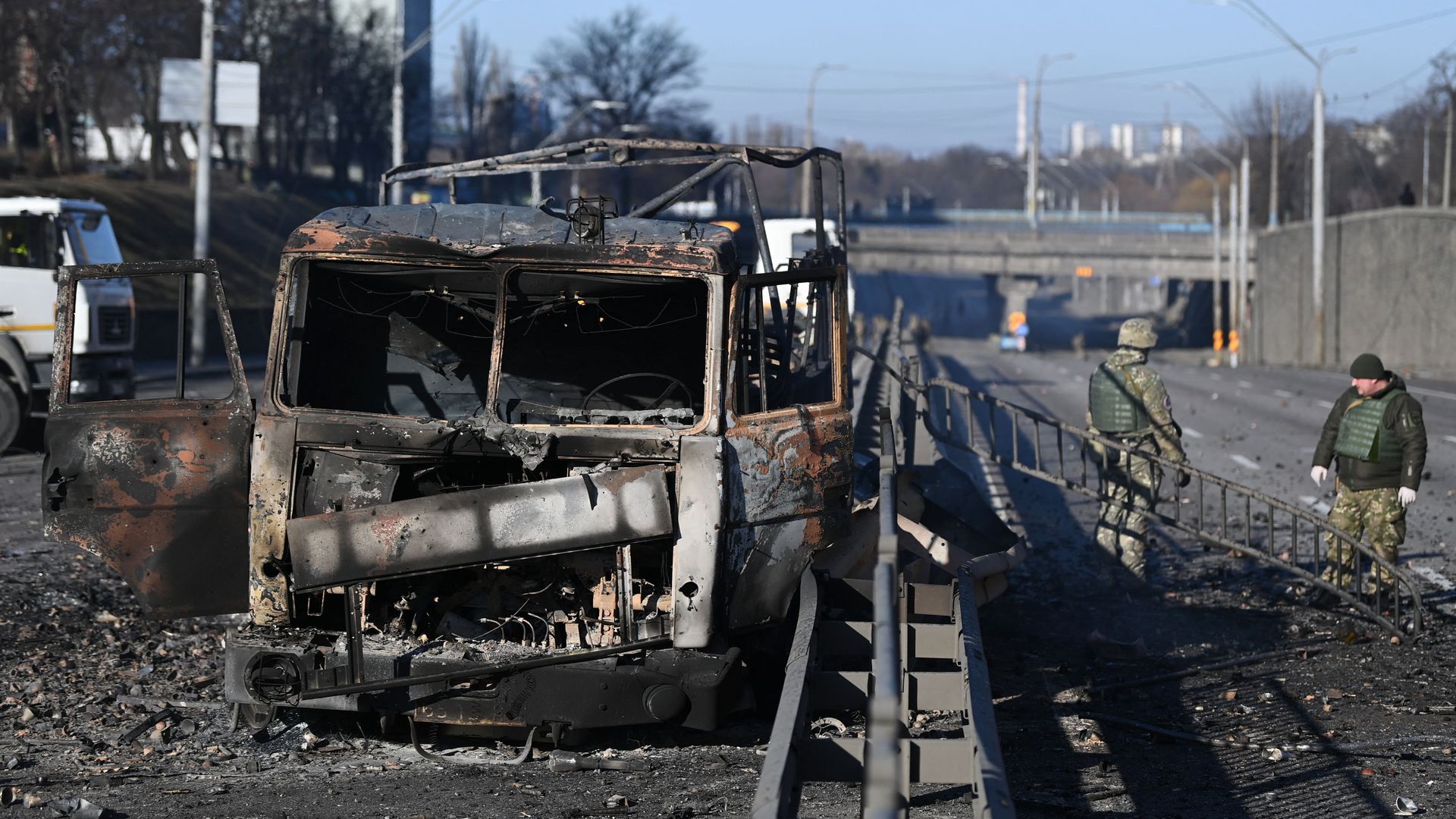 Ukrainian soldiers stand past a burnt Ukrainian army vehicle in Kyiv.