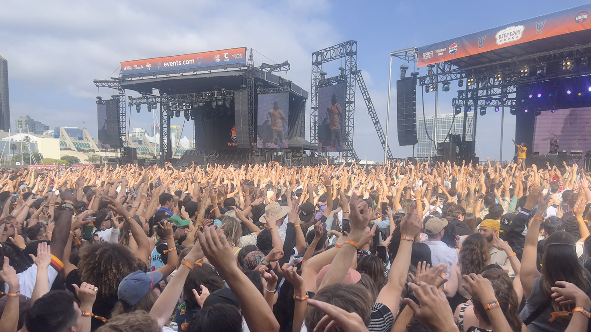 A crowd of people raises their hands in front of stages positioned on San Diego's downtown waterfront