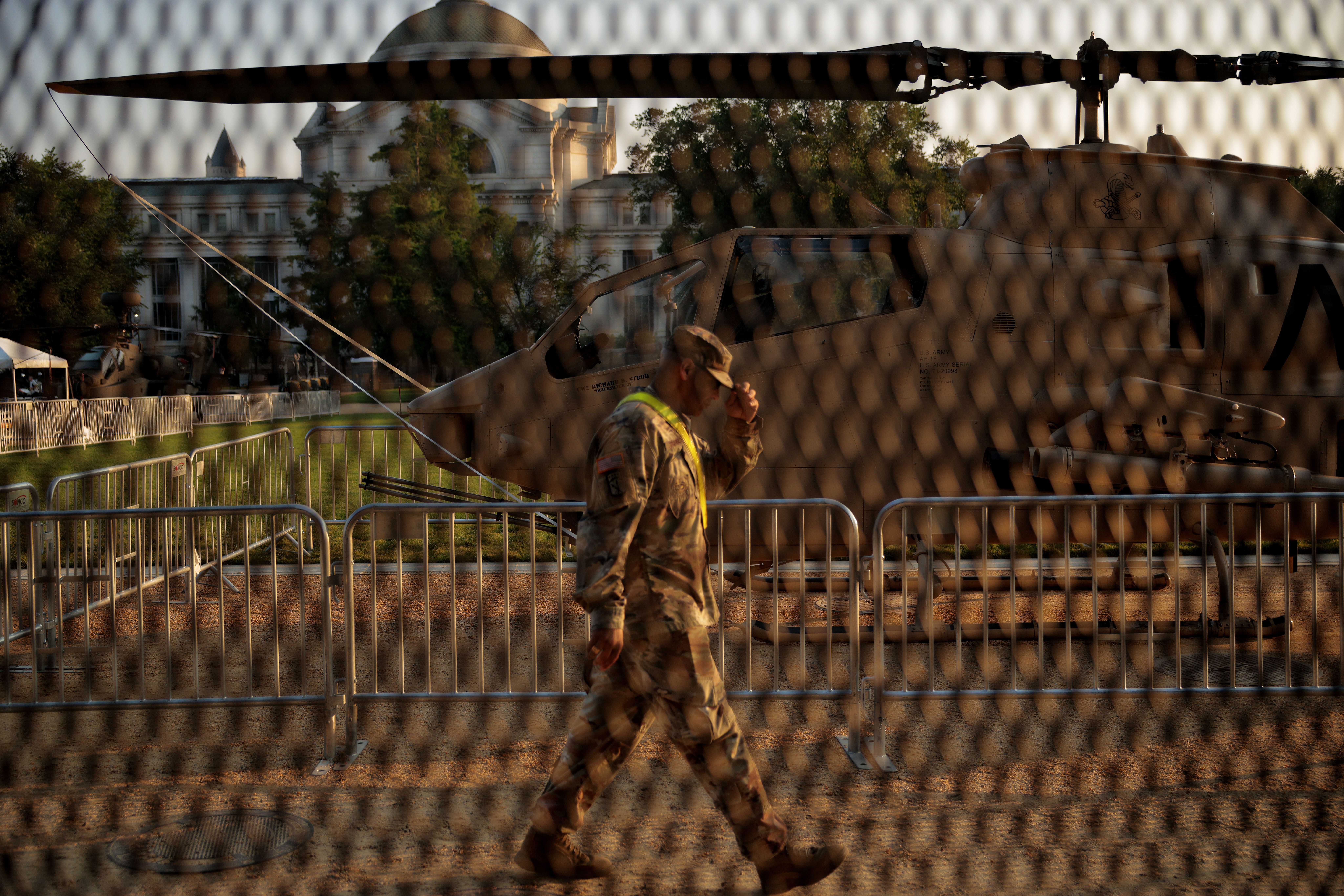 A photo showing a soldier walking behind fencing on Washington, D.C.'s National Mall, with a helicopter in the background.