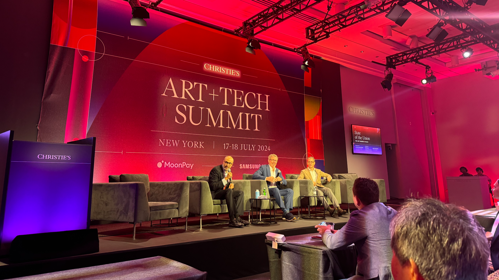 A stage with men sitting in front of a marquee reading Christie's Art + Tech Summit 