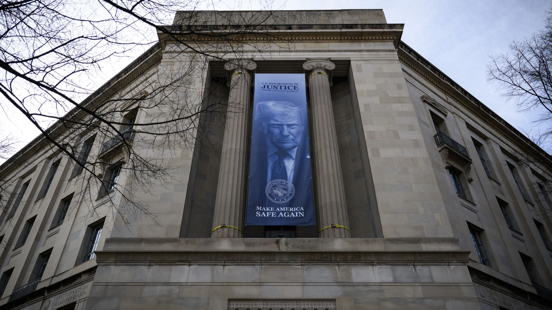 A large banner displaying President Donald Trump hangs from the front of the U.S. Department of Justice headquarters in Washington, D.C.